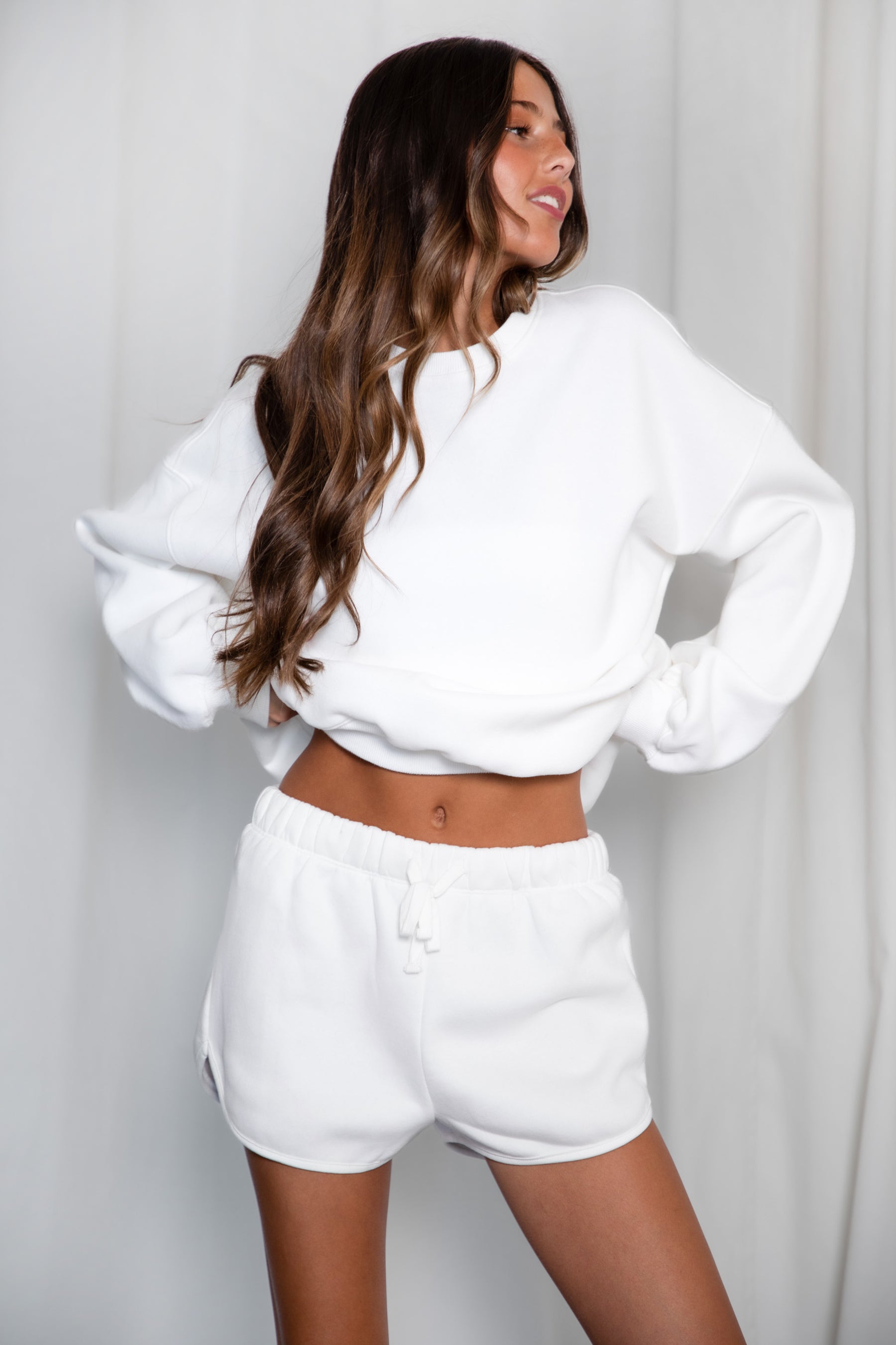 Woman wearing a white sweatshirt and shorts set against a plain background