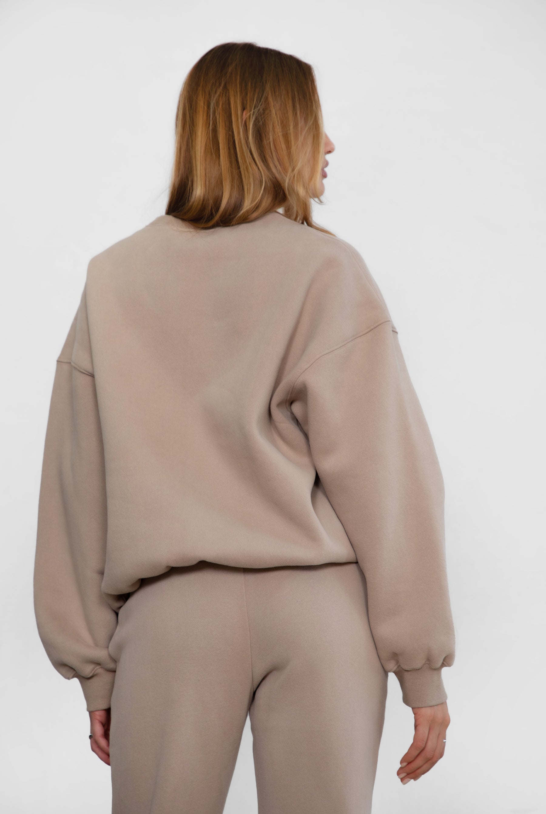 Person wearing a taupe sweater and pants set on a white background