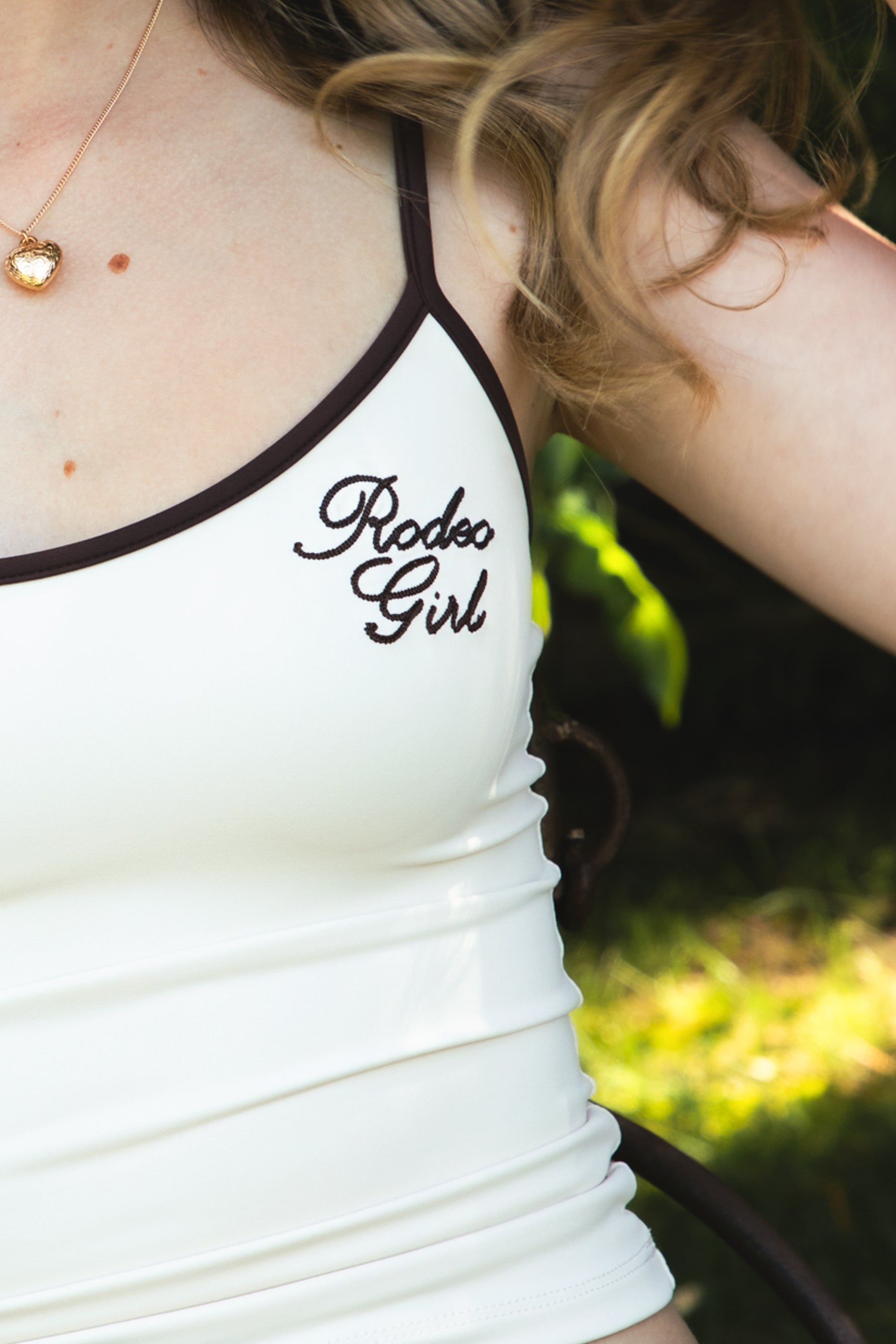 Woman wearing RODETTE soft stretch lettering crop tank top featuring contrast shoulder straps and neckline, brushed stretch nylon fabric, Rodeo Girl embroidered chest detail, adjustable thin straps, and a body-hugging cropped silhouette for western-inspired casual styling.