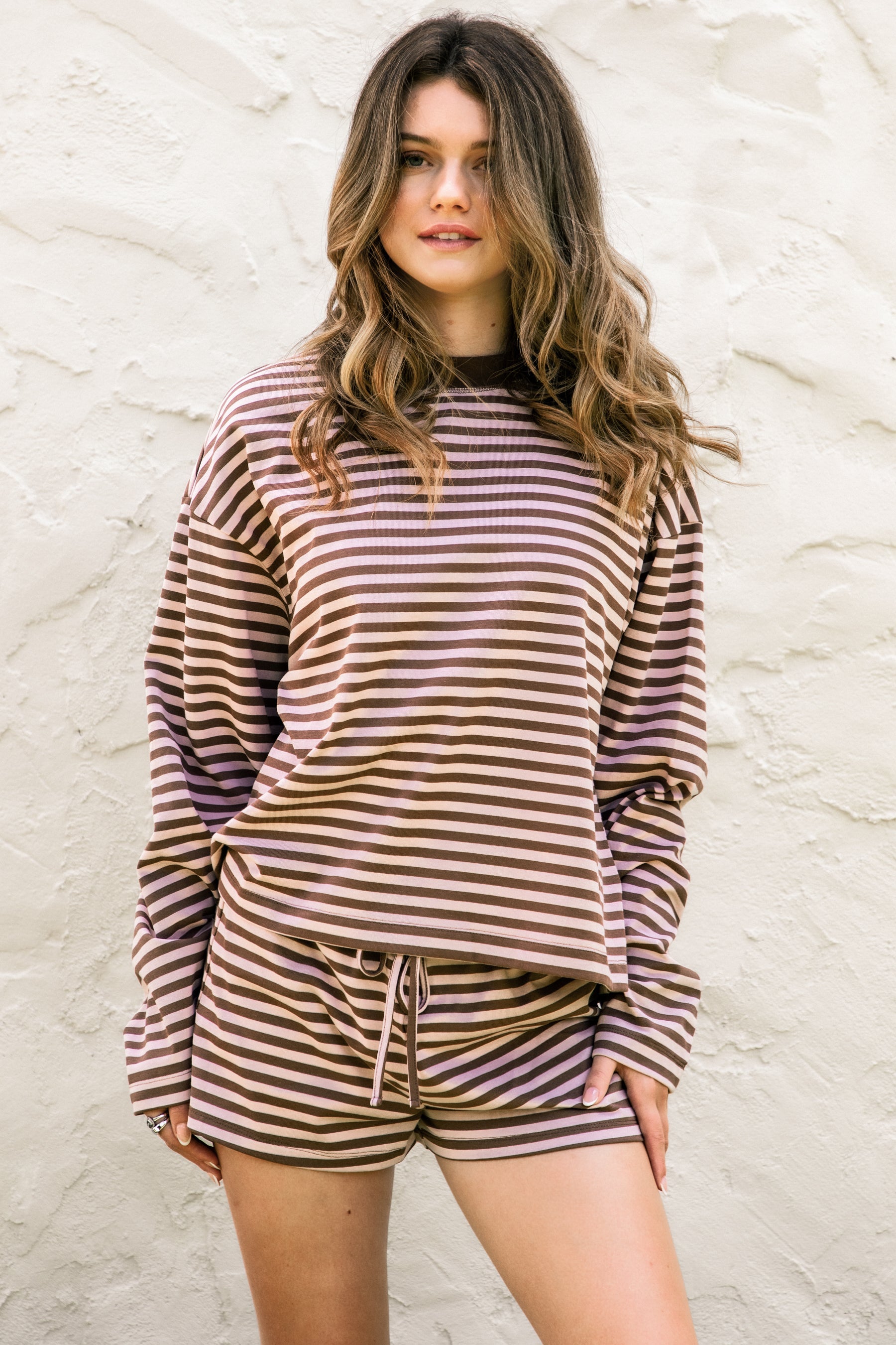 Woman wearing TIC TOC TH31849 MARLOWE striped long sleeve top with a classic crew neckline, relaxed semi-oversized fit, easy drop shoulders, and soft horizontal stripes paired with dark denim jeans in a casual outdoor street setting.