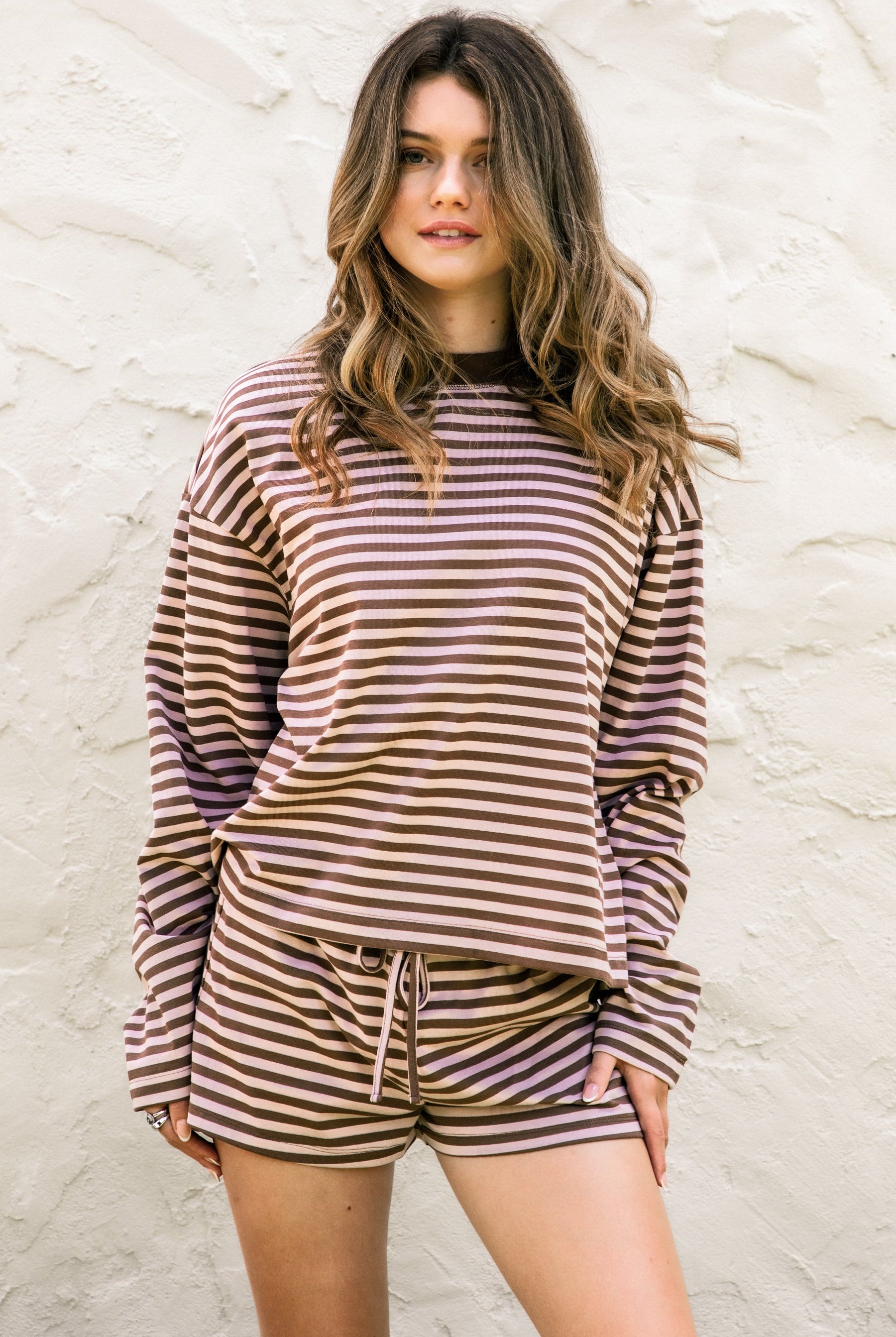 Woman wearing TIC TOC TH31849 MARLOWE striped long sleeve top with a classic crew neckline, relaxed semi-oversized fit, easy drop shoulders, and soft horizontal stripes paired with dark denim jeans in a casual outdoor street setting.
