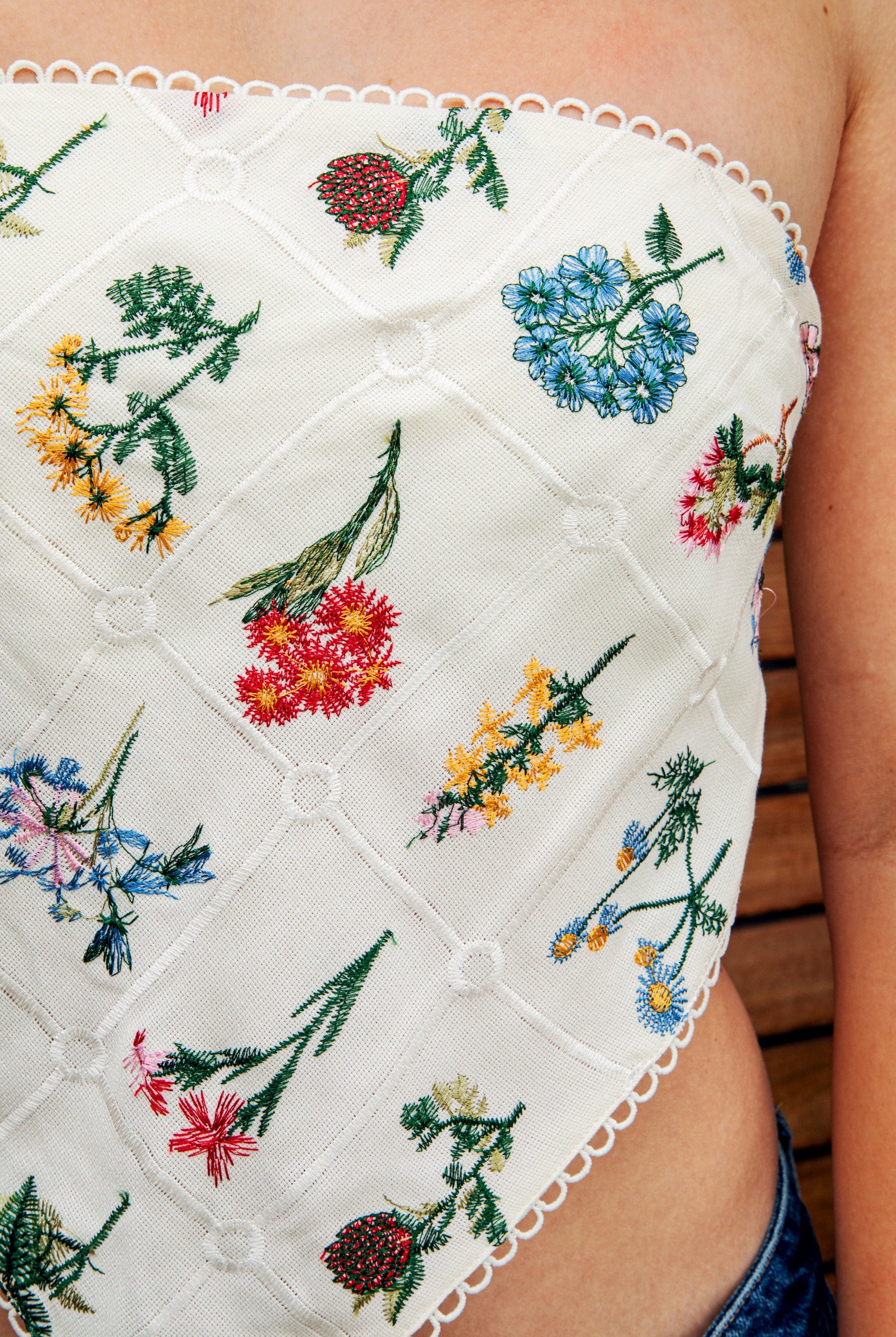 Woman wearing FLORELLE floral embroidered bandana crop tank top featuring delicate floral embroidery on textured linen blend fabric, classic cropped bandana silhouette, adjustable self tie back, and scalloped picot trim for summer resort and festival styling.