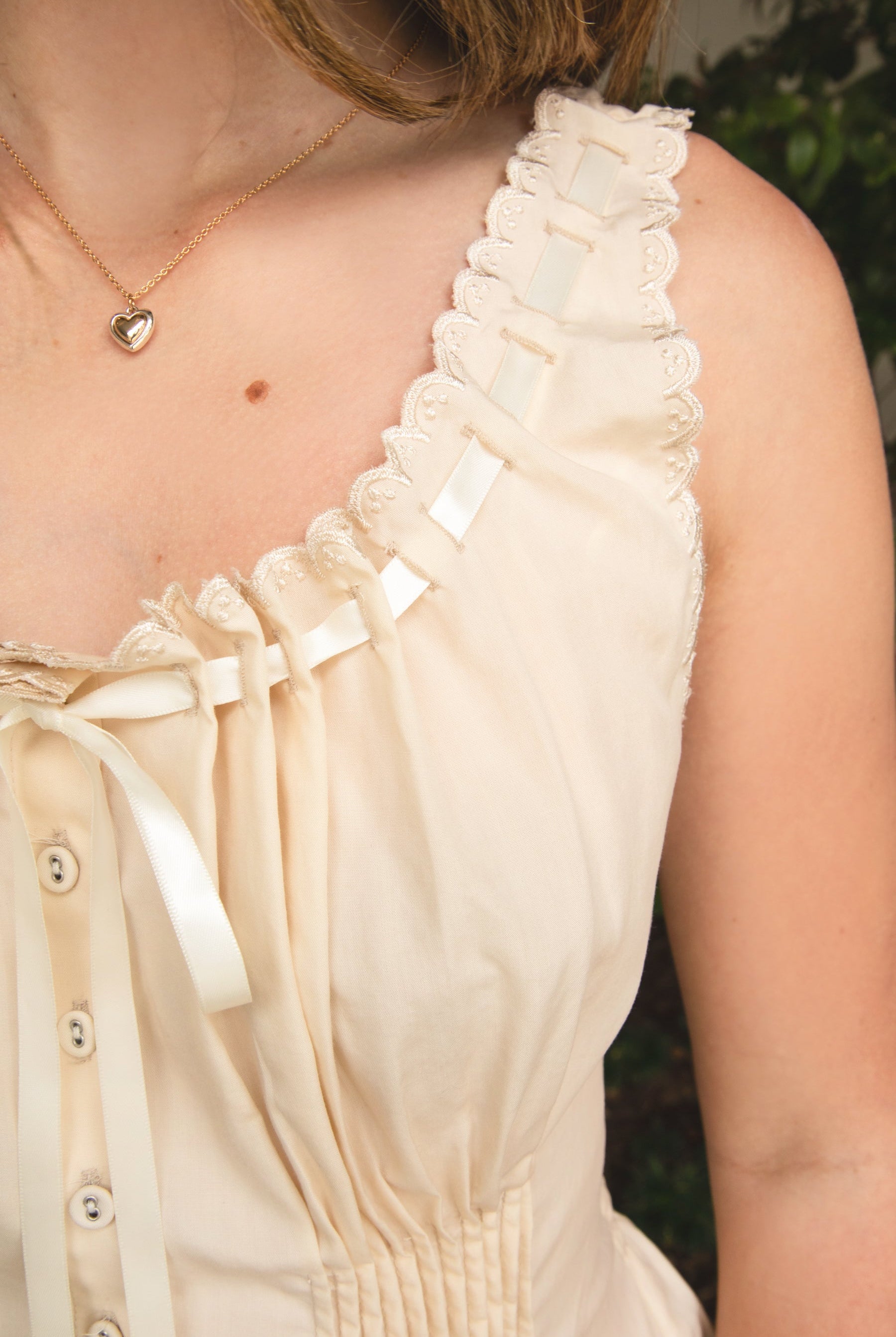 Woman wearing LENA smocked ribbon tie peplum tank top featuring a romantic scoop neckline with scalloped lace trim, front ribbon tie and button detail, smocked waist, wide shoulder straps with satin ribbon loop accents, and soft lightweight lyocell fabric.