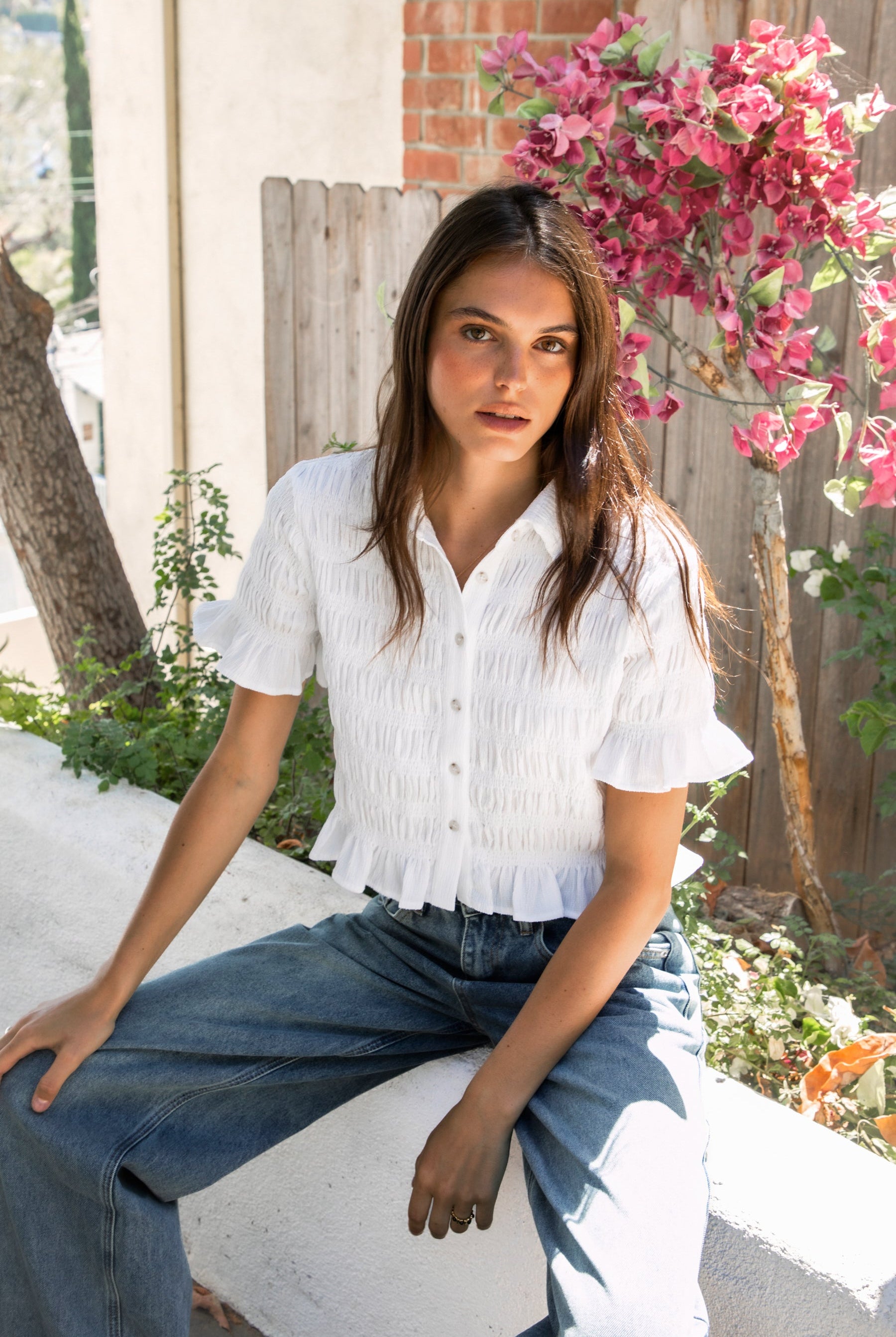 Woman wearing LISETTE smocked button front collared crop top featuring allover smocked textured fabric, soft stretch fit, classic collared neckline, functional button front closure, short puff sleeves with flounce ruffle cuffs, and a cropped silhouette with delicate ruffle hem.