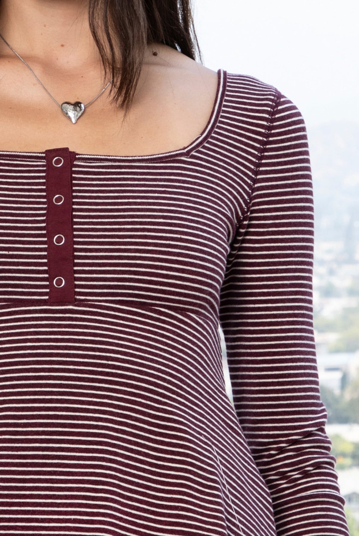 Woman wearing ELODY striped babydoll square neck henley peplum top featuring soft striped knit fabric, wide scoop neckline with contrast trim, henley inspired front placket with metal snap details, fitted bodice, empire waist seam, flared peplum hem, and long fitted sleeves.