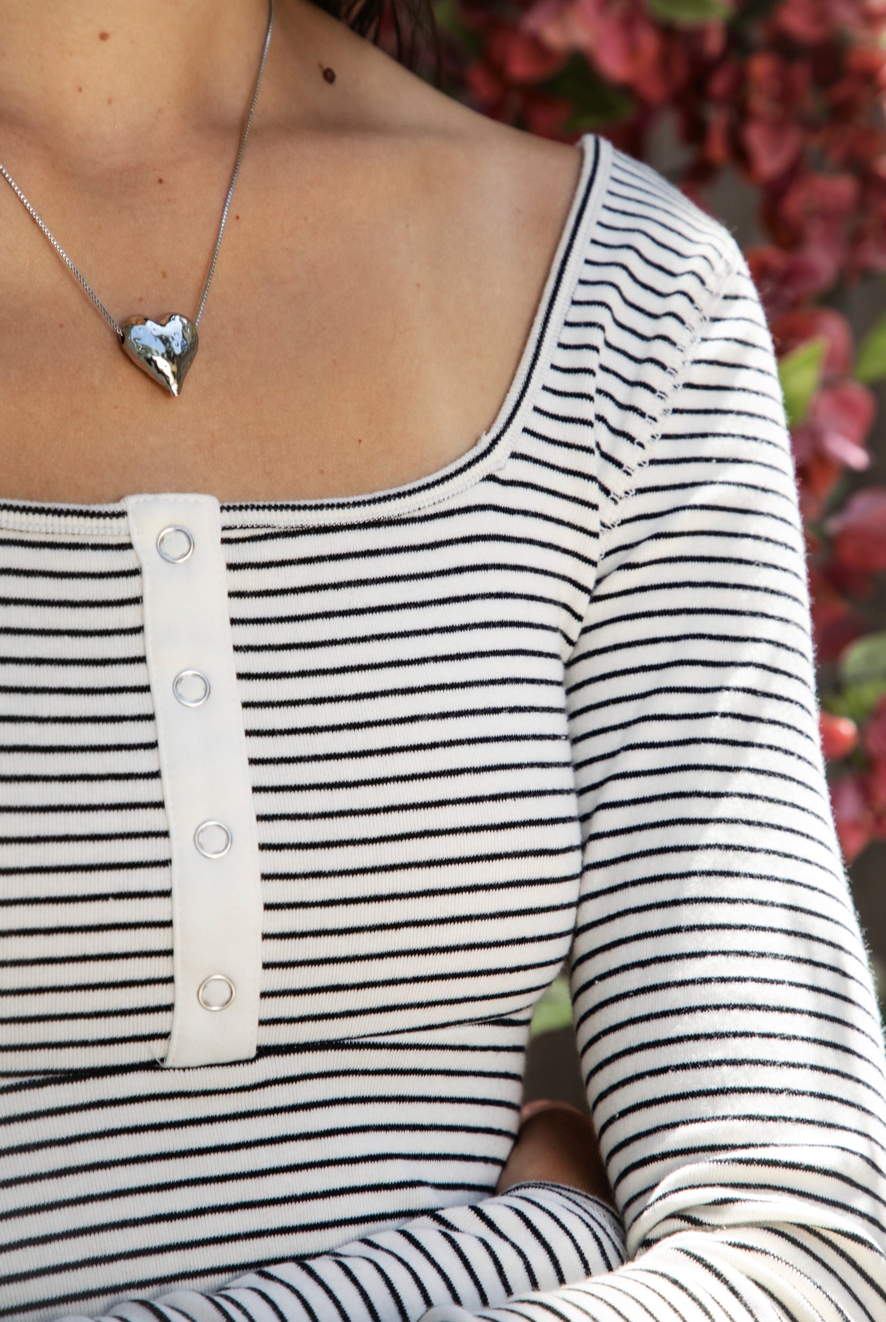 Woman wearing ELODY striped babydoll square neck henley peplum top featuring soft striped knit fabric, wide scoop neckline with contrast trim, henley inspired front placket with metal snap details, fitted bodice, empire waist seam, flared peplum hem, and long fitted sleeves.