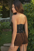 Woman wearing TIC TOC TA31359 BENETTI Black Stretch Poplin Strapless Western Top Black with Bolo Tie paired with suede brown shorts outdoors.