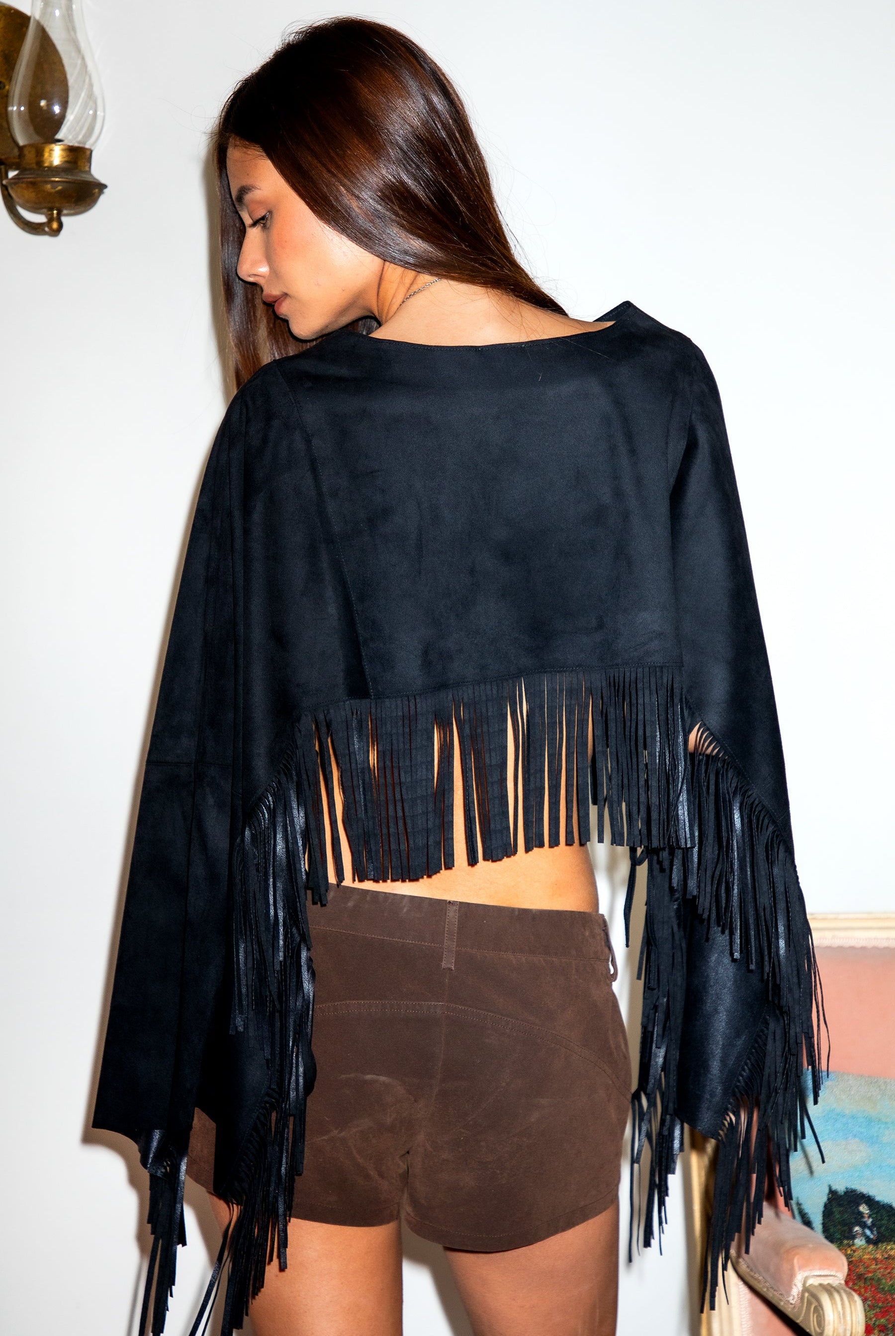 Woman wearing TIC TOC TL31825 STALLION faux suede fringe poncho featuring a cropped cape silhouette, drop shoulder relaxed fit, long fringe tassel detailing along the hem and sleeves, and a soft western-inspired faux suede texture, styled over a fitted top with denim bottoms for a rodeo festival look.