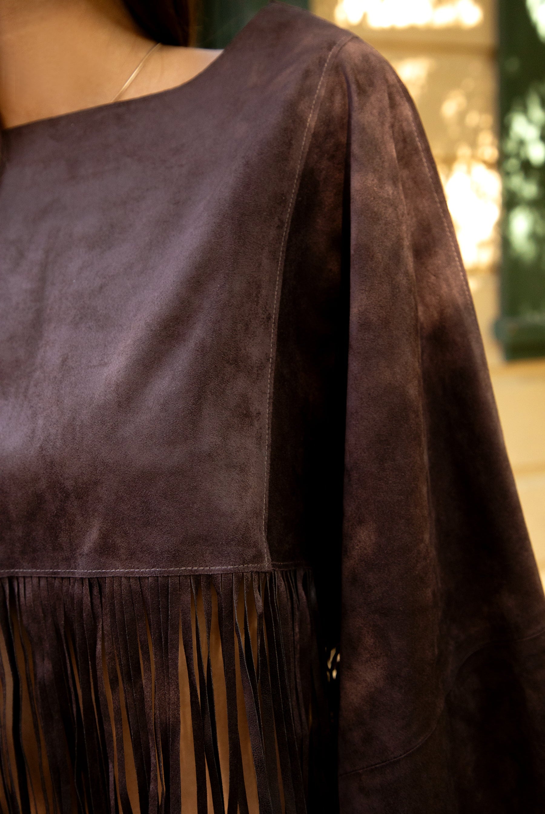 Woman wearing TIC TOC TL31825 STALLION faux suede fringe poncho featuring a cropped cape silhouette, drop shoulder relaxed fit, long fringe tassel detailing along the hem and sleeves, and a soft western-inspired faux suede texture, styled over a fitted top with denim bottoms for a rodeo festival look.