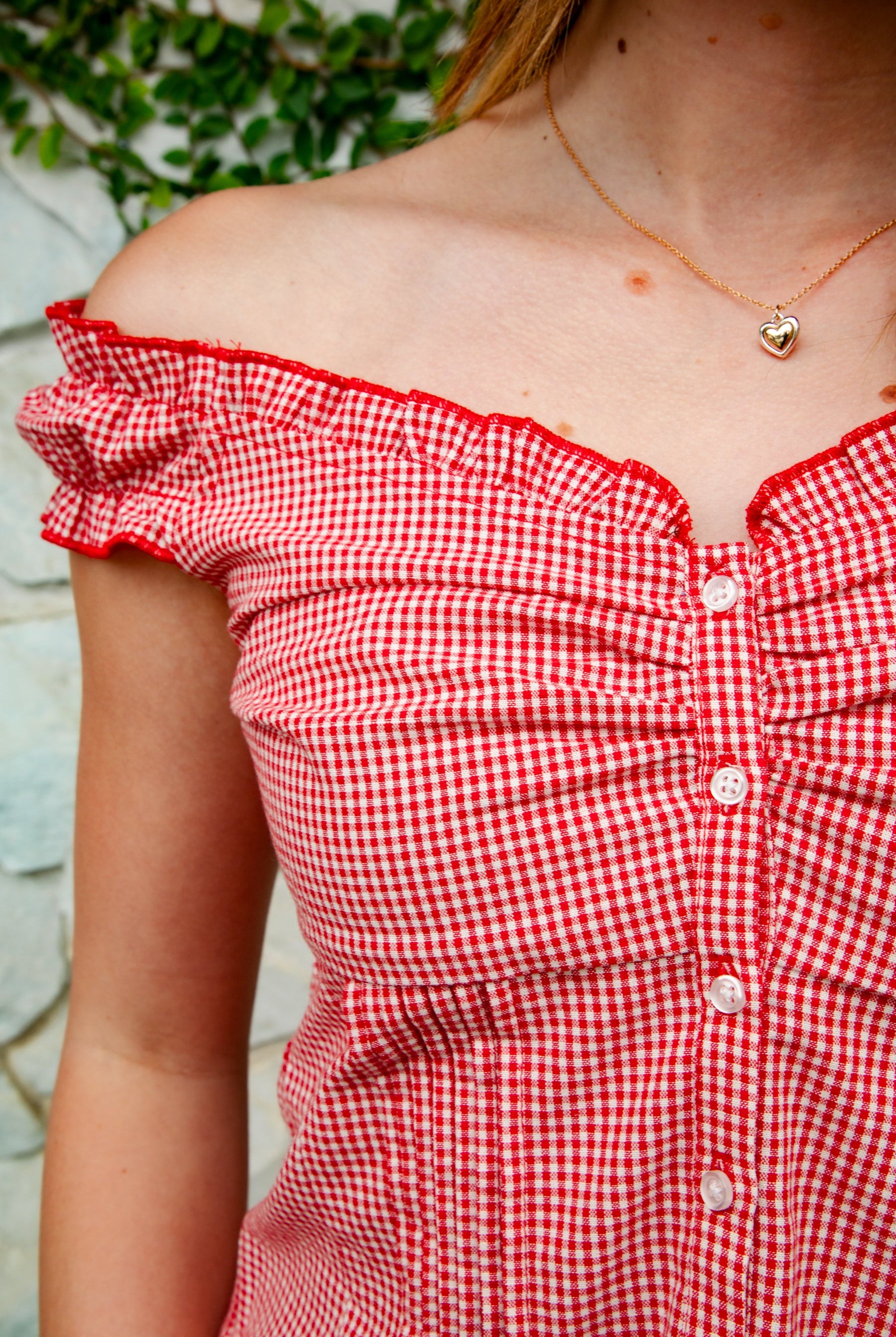 Woman wearing MAREN gingham off shoulder ruffle cap sleeve top featuring a soft ruffle neckline, ruched bust detail, functional button front, smocked back panel, ruffled peplum hem, and lightweight cotton gingham fabric for feminine summer styling.