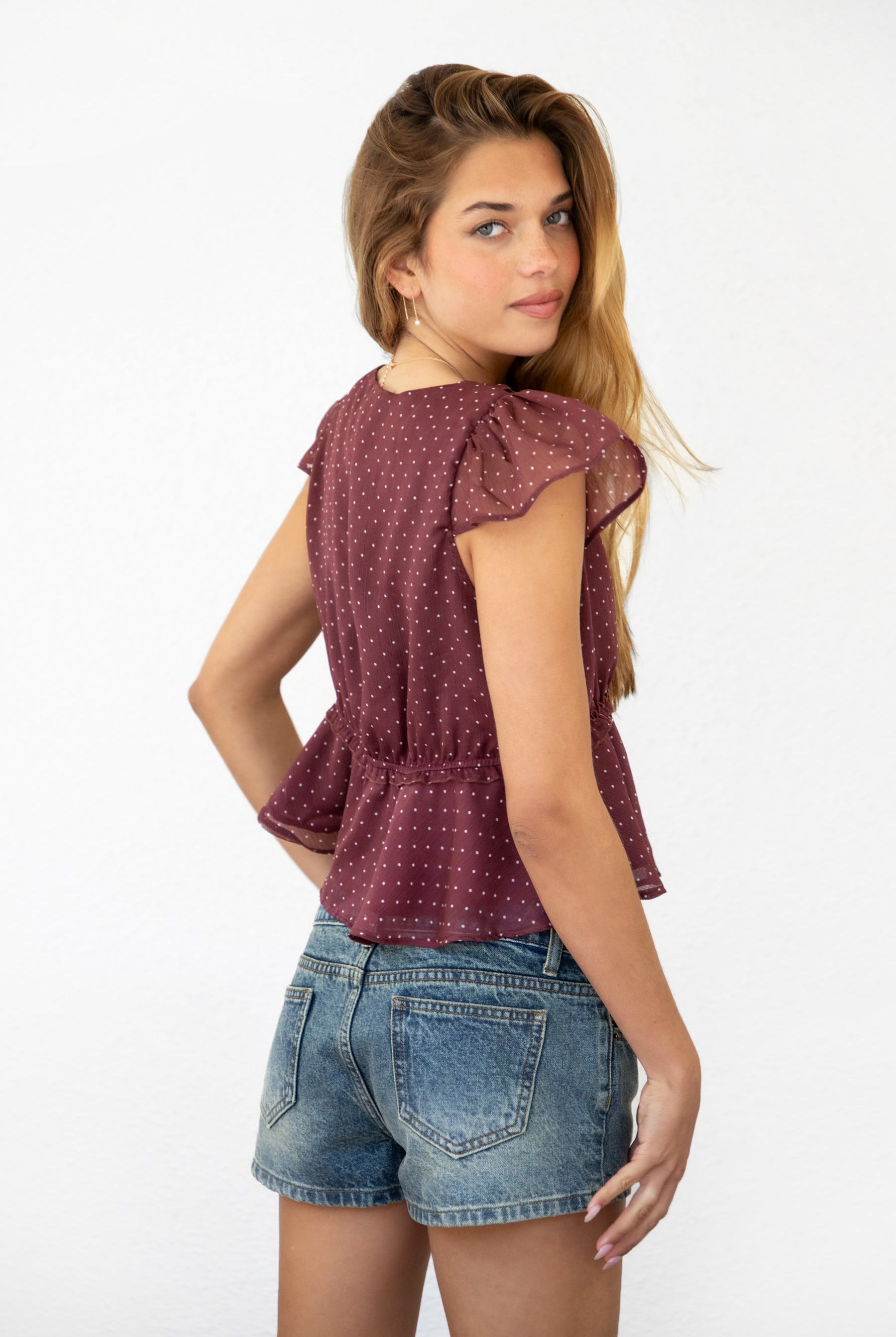 Woman wearing WYNONA polka dot chiffon crop top featuring lightweight printed chiffon, V-neckline with ruffle trim, flutter sleeves, elastic underbust band, front bow detail, and a cropped peplum silhouette with full lining for comfort.
