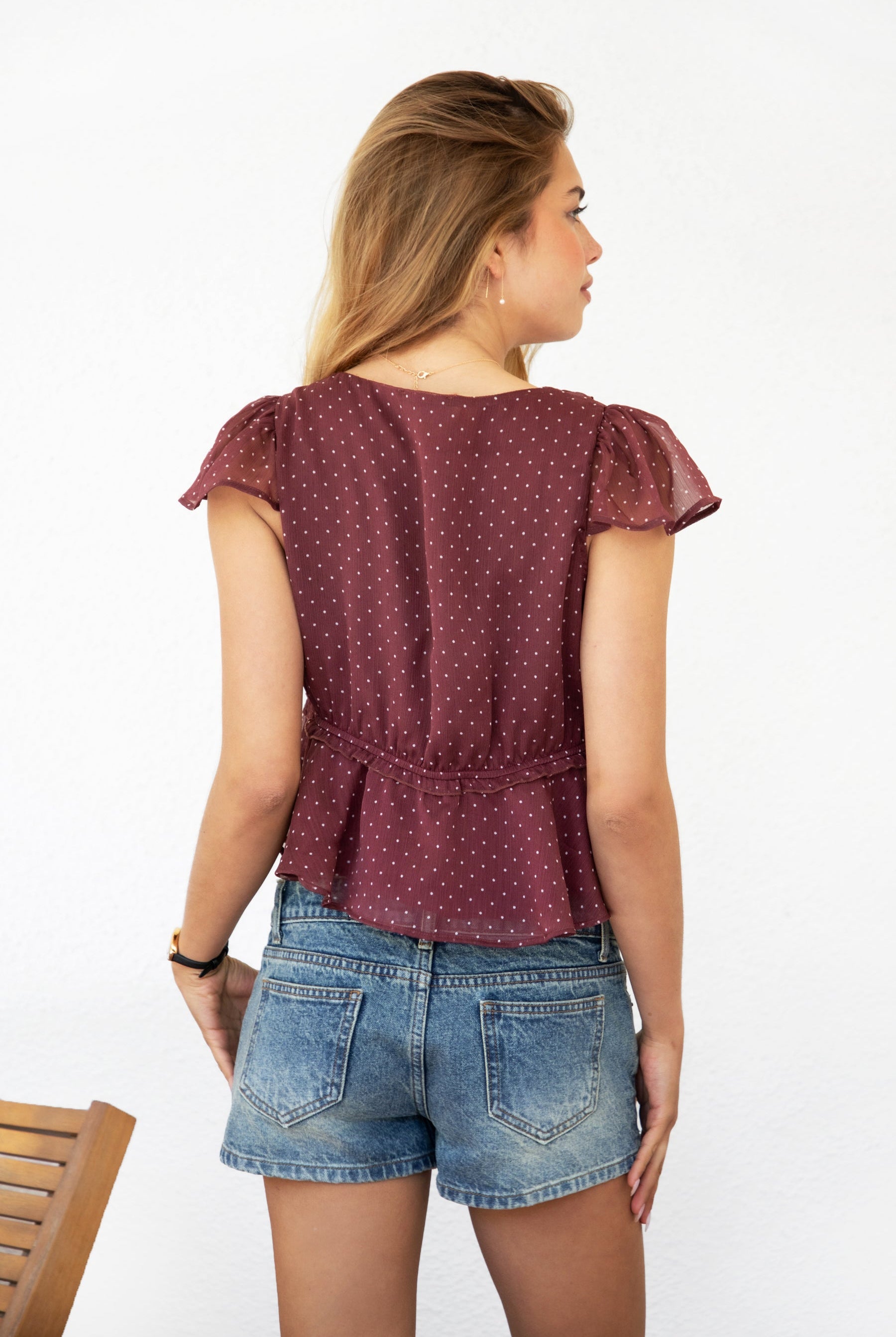 Woman wearing WYNONA polka dot chiffon crop top featuring lightweight printed chiffon, V-neckline with ruffle trim, flutter sleeves, elastic underbust band, front bow detail, and a cropped peplum silhouette with full lining for comfort.