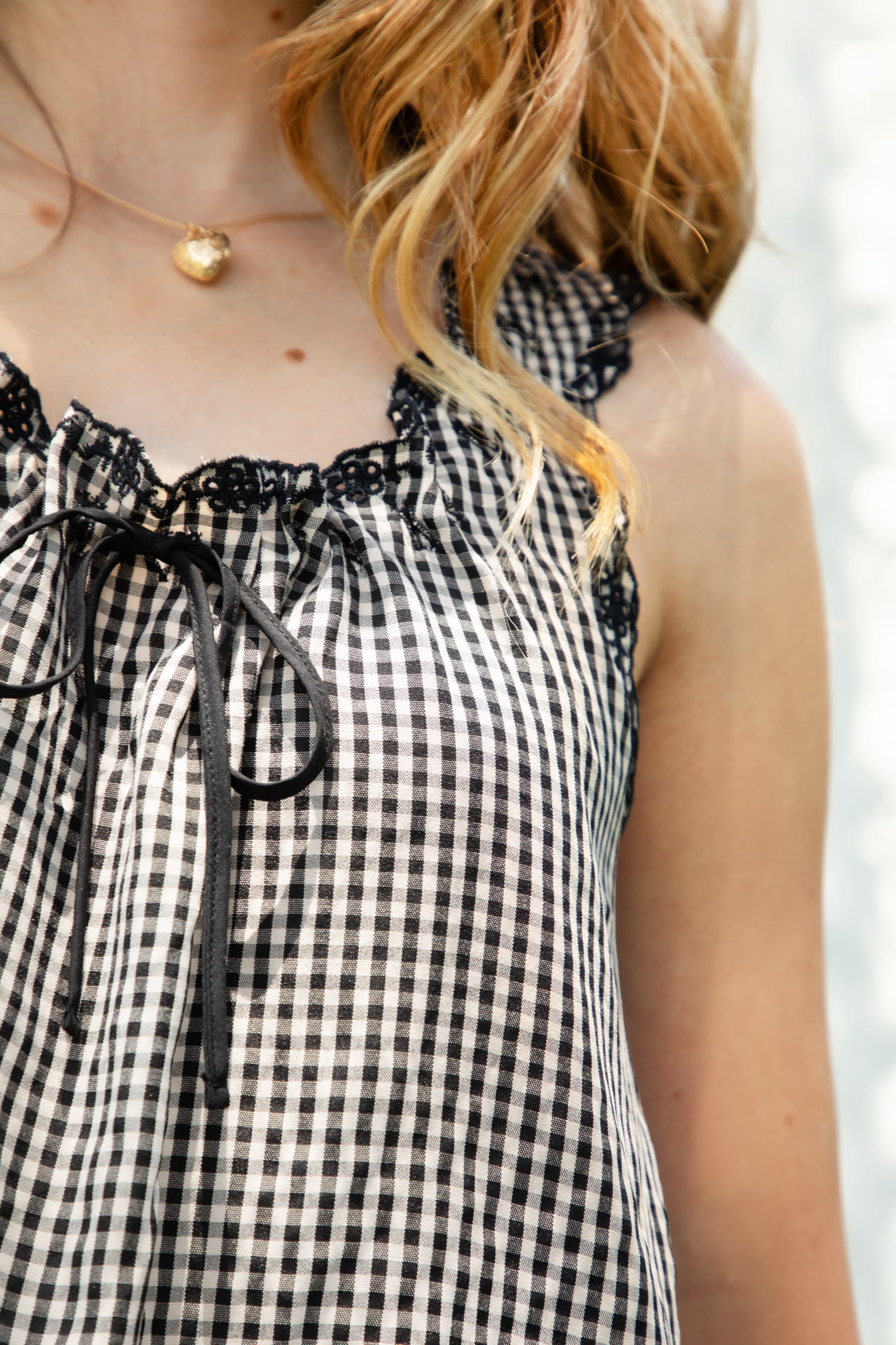 Woman wearing PRAIRELLE gingham embroidered sleeveless top and shorts set featuring a sweet gingham print, delicate floral embroidery lace trim, front self tie bow detail, matching elastic waist shorts, scalloped lace hem, and lightweight rayon fabric for relaxed summer styling.