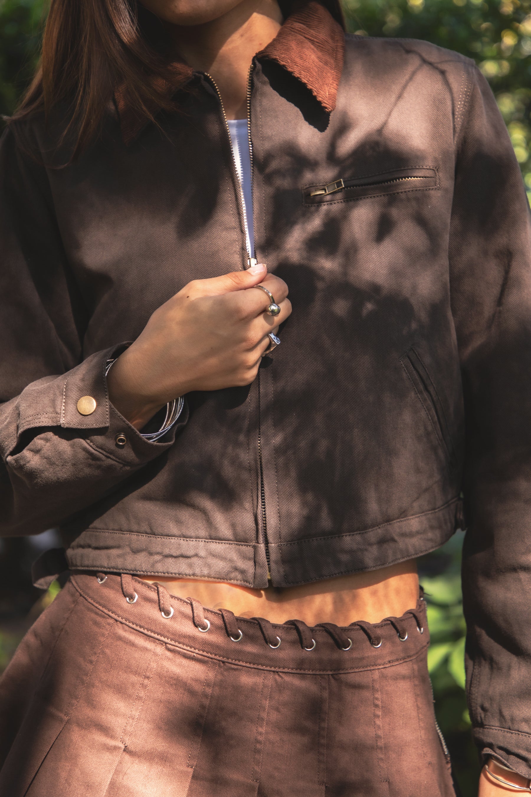 Woman wearing TIC TOC TT31861-FLINT FLINT washed solid twill cropped jacket featuring a front zip closure, contrast brown corduroy collar, two side pockets, a single chest zip pocket, snap button cuffs, and side buckle strap detail at the waistline, with satin quilted lining and light padding, styled over a simple top and denim for a western-inspired everyday transitional look.