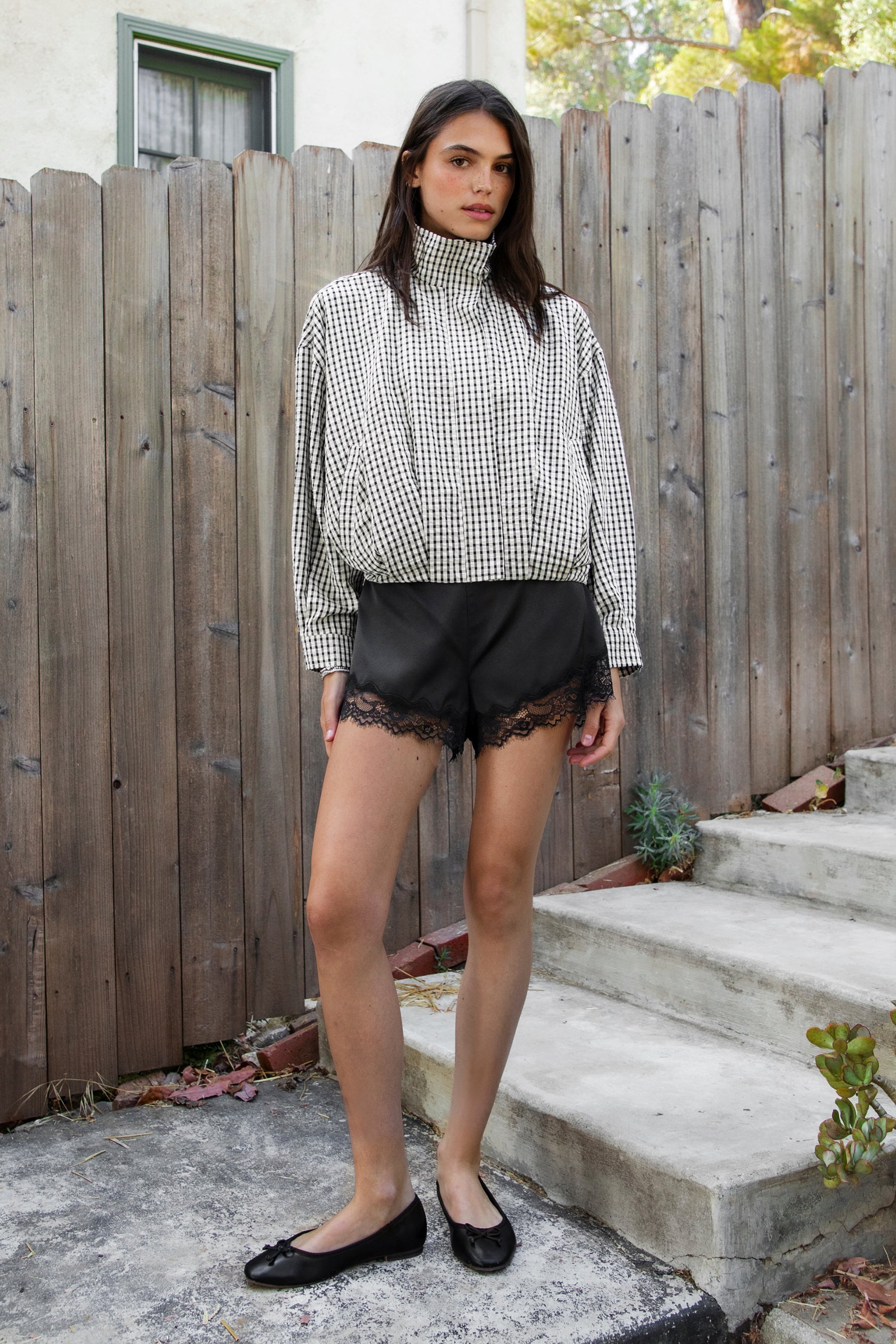 Woman wearing MARGOT plaid gingham zip up bomber jacket featuring lightweight crinkled cotton blend fabric, classic gingham plaid pattern, high neck collar, front button and zip closure, semi cropped length, sleeve snap buttons, relaxed drop shoulder silhouette, side pockets, and elastic hem.