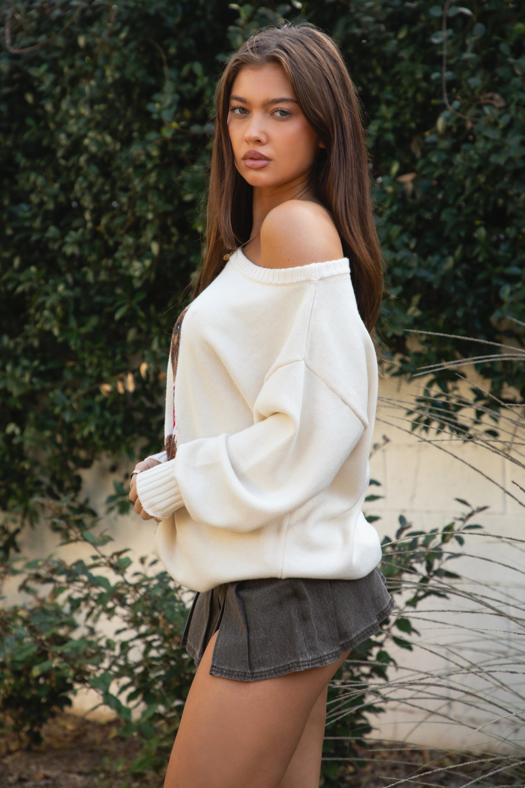 Woman wearing TIC TOC TV31893-MALTIE MALTIE knit sweater featuring a wide boat off-the-shoulder neckline, oversized relaxed fit, dropped shoulders, and long sleeves with ribbed cuffs, showcasing a poodle intarsia front graphic with American flag detailing, styled casually with denim for a cozy Americana-inspired weekend look.