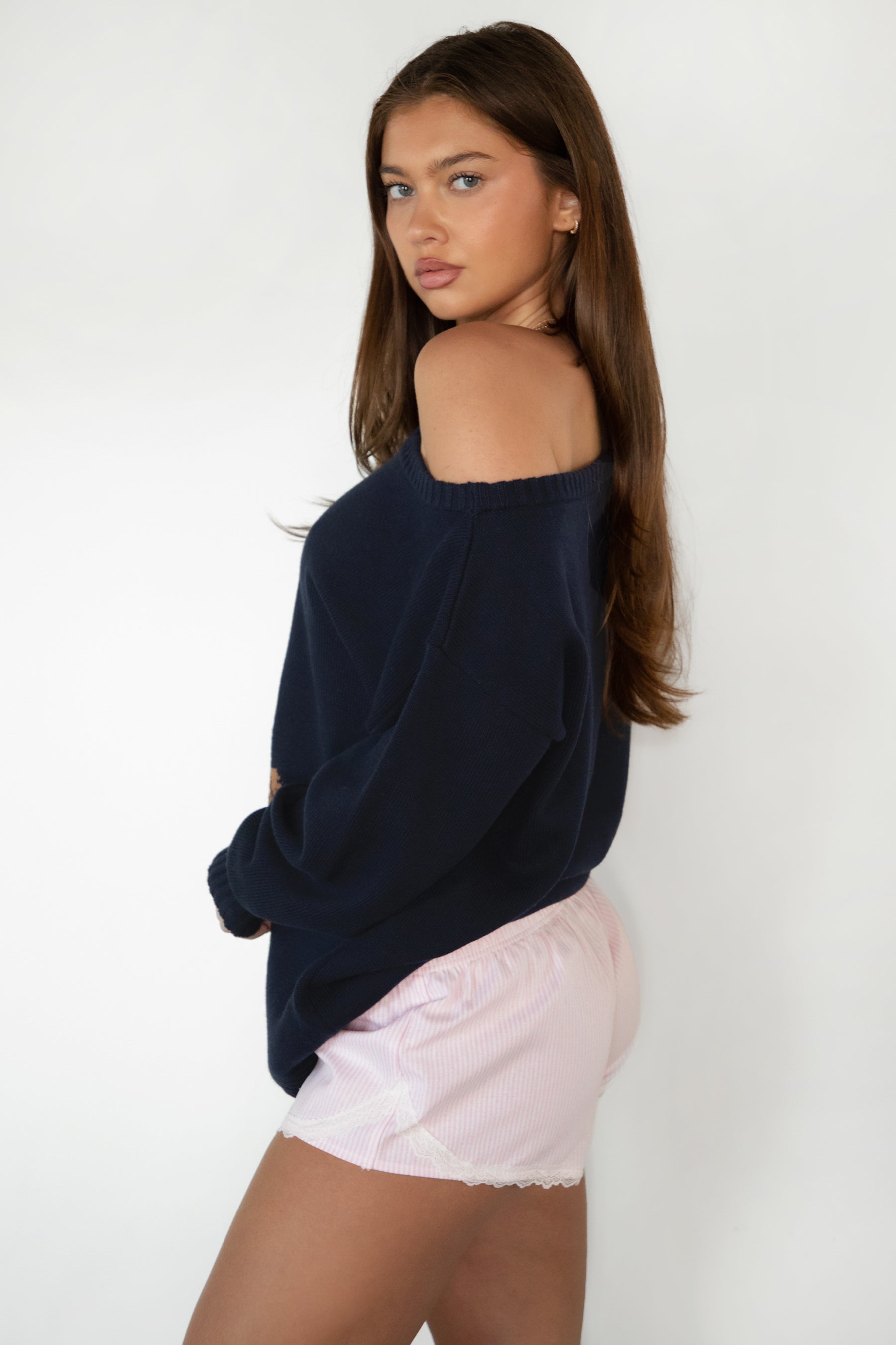 Woman wearing TIC TOC TV31893-MALTIE MALTIE knit sweater featuring a wide boat off-the-shoulder neckline, oversized relaxed fit, dropped shoulders, and long sleeves with ribbed cuffs, showcasing a poodle intarsia front graphic with American flag detailing, styled casually with denim for a cozy Americana-inspired weekend look.