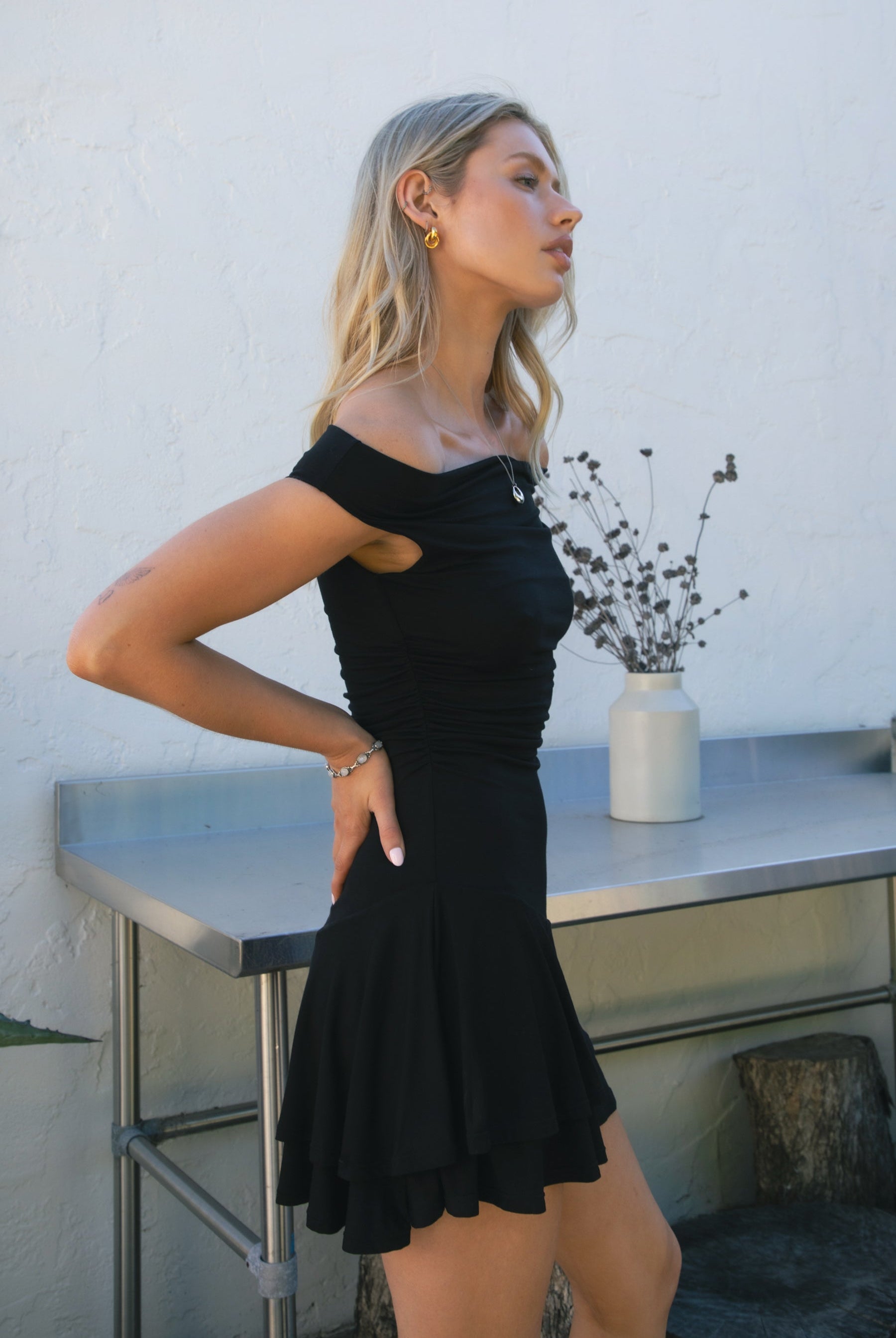 Woman wearing TIC TOC DC31642BA RAVAYA off-the-shoulder mini dress featuring ruched sides and a frill hemline in soft rayon spandex fabric