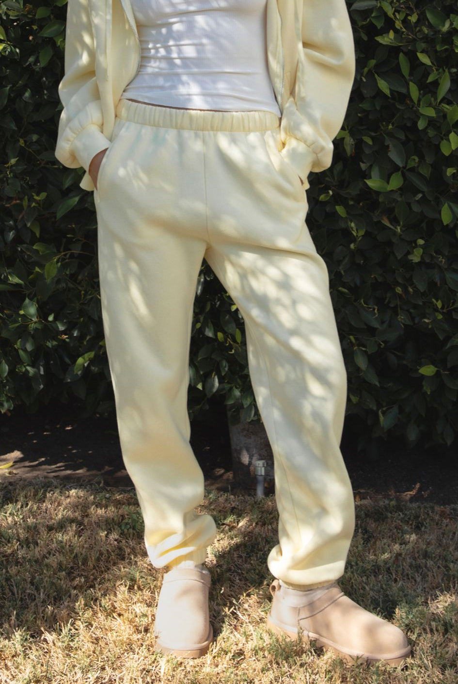 Woman wearing the TIC TOC PH26027 DOVE pale yellow high waist sweatpants featuring an elastic waistband, deep side pockets, and tapered ankle hem with a matching top.