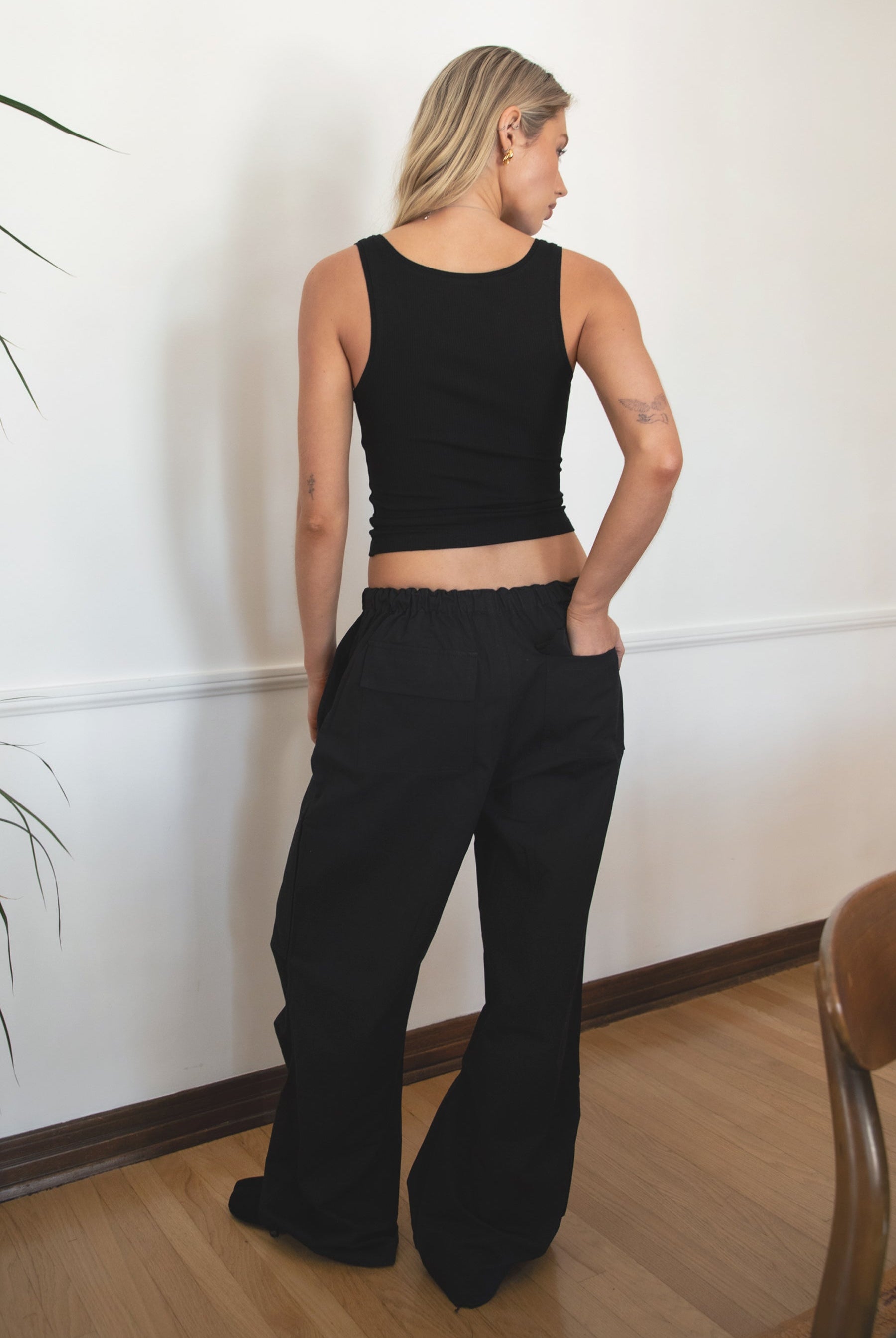 Woman wearing TIC TOC PH28246 GENIE black parachute twill pants featuring adjustable waistband, relaxed wide-leg fit, and drawstring hems. against a white wall.
