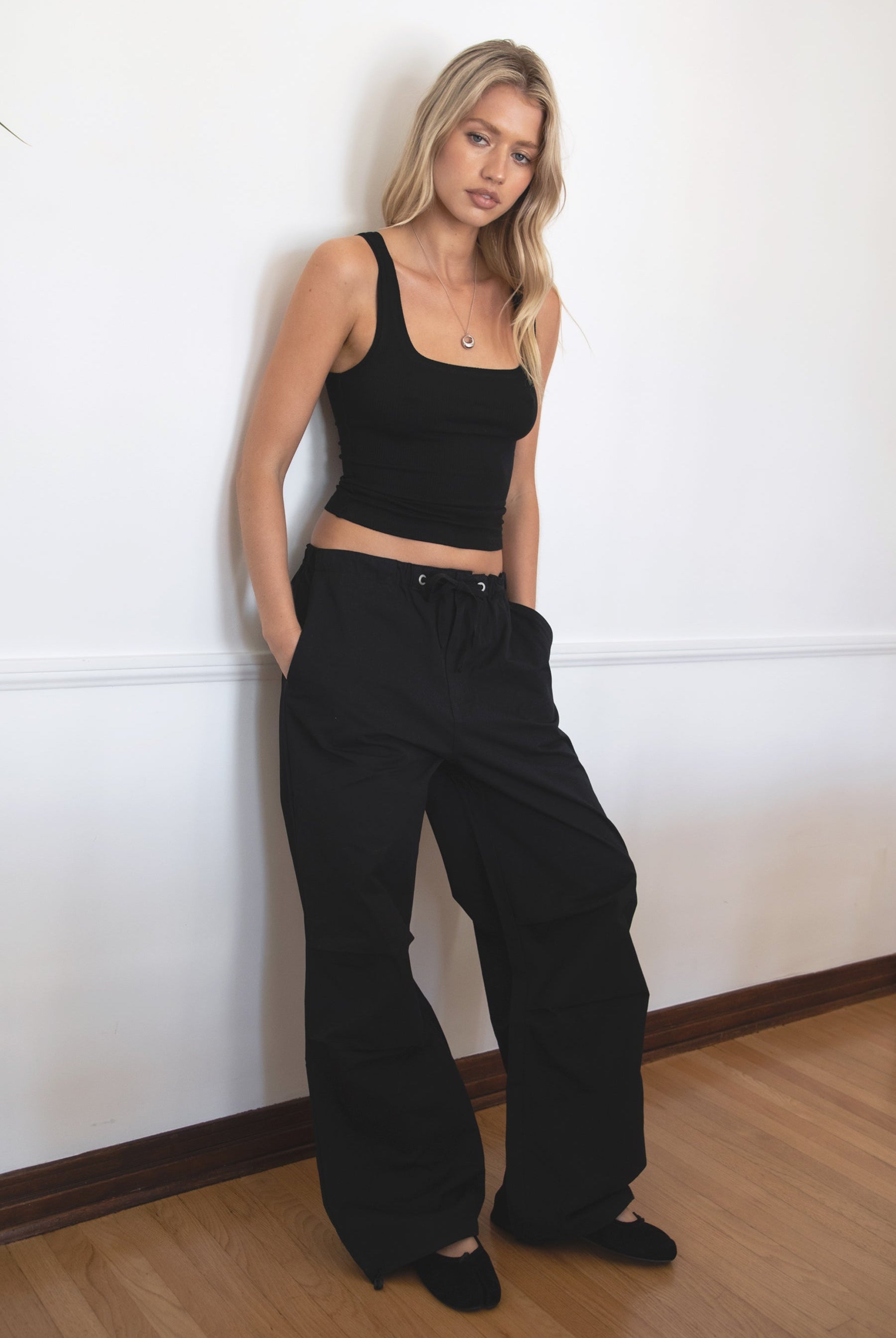 Woman wearing TIC TOC PH28246 GENIE black parachute twill pants featuring adjustable waistband, relaxed wide-leg fit, and drawstring hems. against a white wall.
