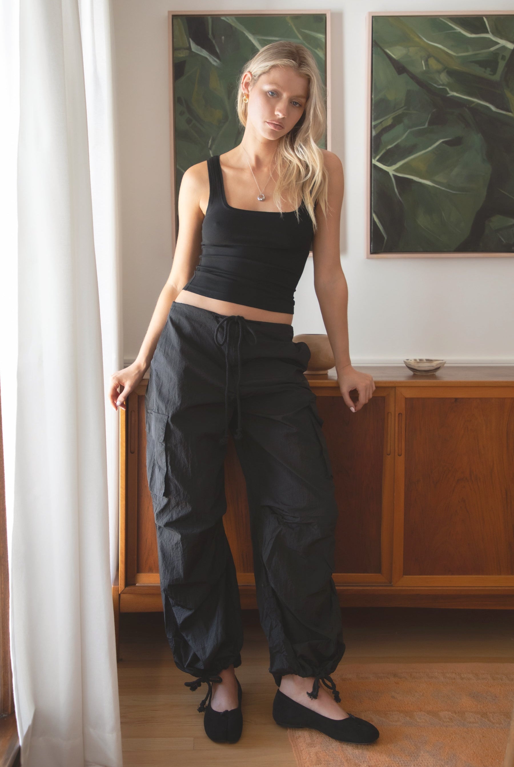 Woman wearing a black tank top and TIC TOC PH29131 TOMY black crinkled nylon parachute cargo pants with adjustable drawstring waistband and wide-leg silhouette indoors