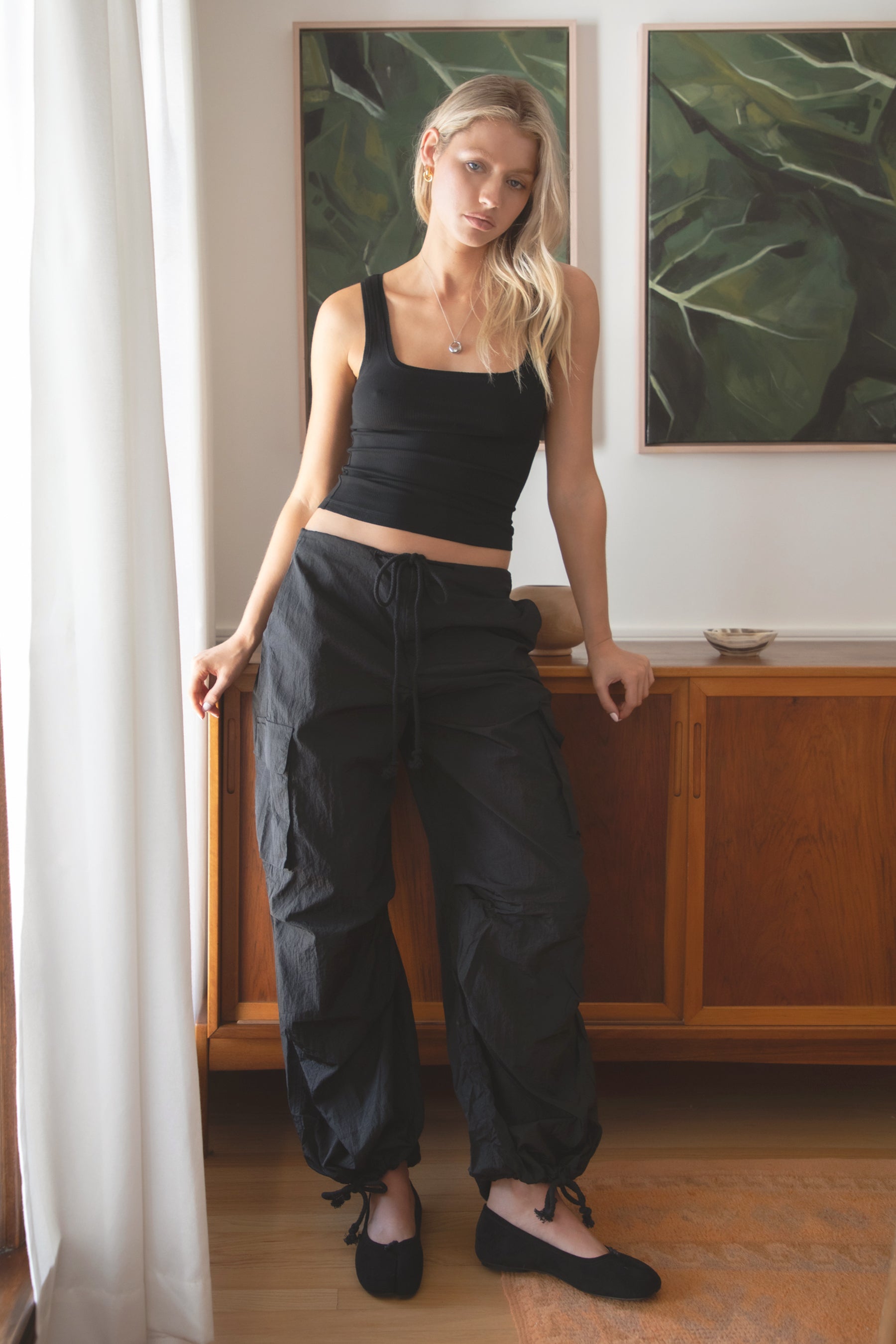 Woman wearing a black tank top and TIC TOC PH29131 TOMY black crinkled nylon parachute cargo pants with adjustable drawstring waistband and wide-leg silhouette indoors