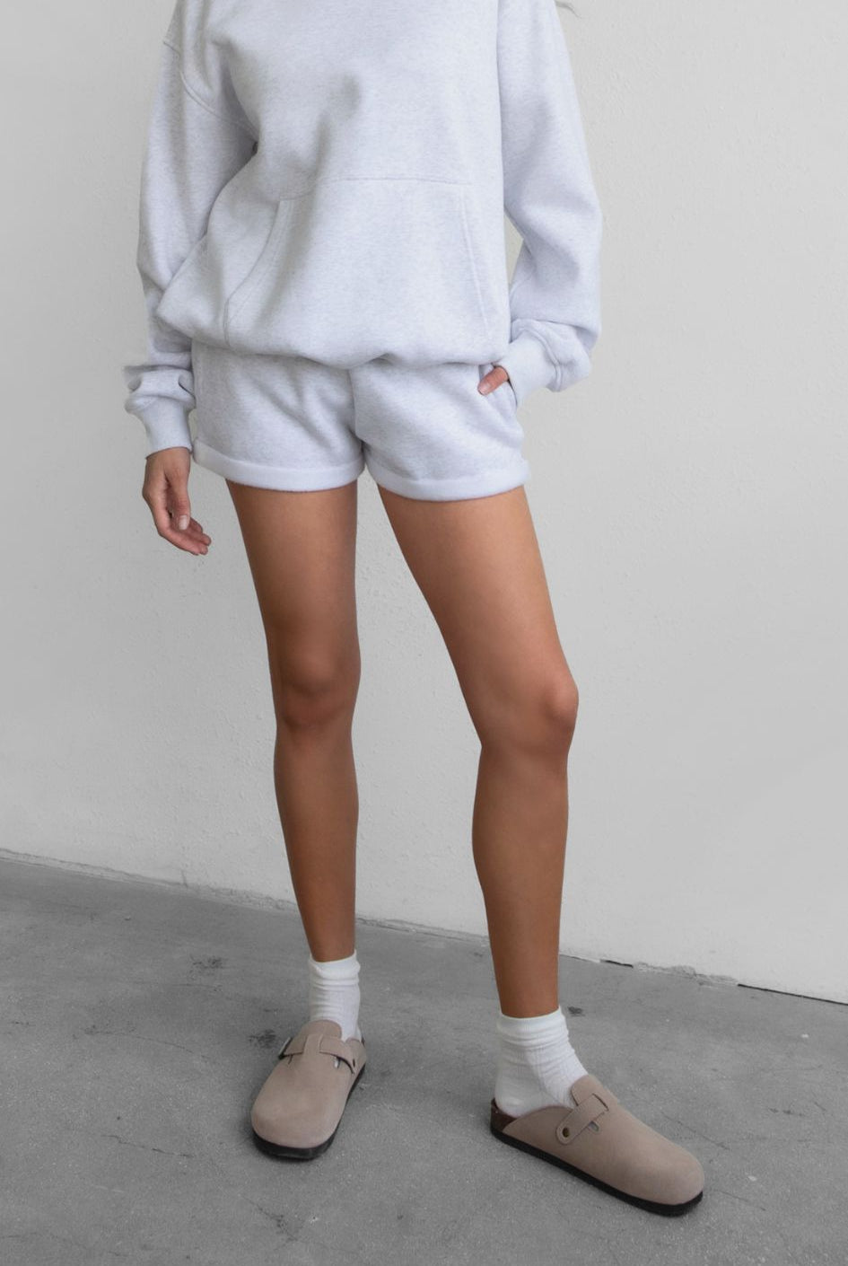 Woman wearing the TIC TOC PJ31004 CARLY ash cloud fleece low rise shorts featuring an elastic waistband with drawcord, deep side pockets, and raw cut hemline paired with a matching top
