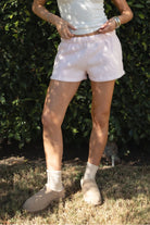 Woman wearing the TIC TOC PJ31004 CARLY pale pink cloud fleece low rise shorts featuring an elastic waistband with drawcord, deep side pockets, and raw cut hemline paired with a white tank top