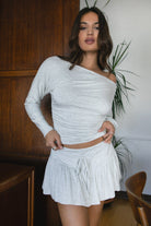 Woman wearing the TIC TOC SC31643BA CHIA heather white mini skirt with built-in shorts featuring drop waist design, frill hem detail, and drawstring waistband paired with the matching top outdoors.
