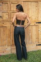 Woman wearing the TIC TOC TA31474 JOSIE faux suede fringe halter top featuring layered fringe neckline, lace trim tie detail, and open back with lace-up closure and dark jeans against a wooden background