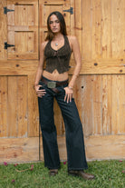 Woman wearing the TIC TOC TA31474 JOSIE faux suede fringe halter top featuring layered fringe neckline, lace trim tie detail, and open back with lace-up closure and dark jeans against a wooden background