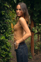 Woman wearing the TIC TOC TA31568 RIVIARA stretch suede western corset top featuring halter neckline, lace-up front, and contrast embroidery with studded trim and dark pants in an outdoor setting.