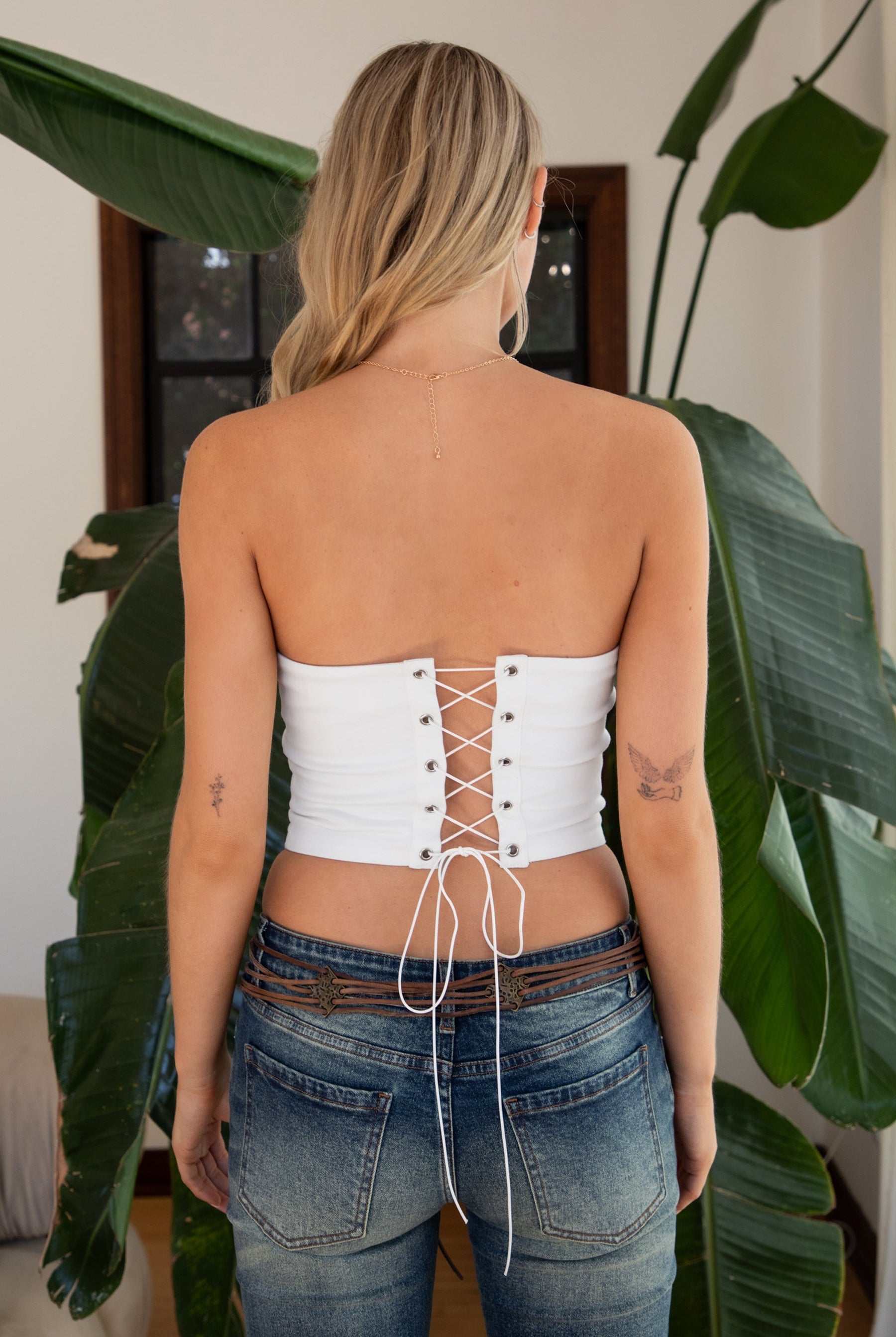 Woman wearing TIC TOC TA31570 HOWDEE white stretch twill strapless bustier top with “Howdy Cowboys” embroidery and rhinestone boot graphic paired with dark denim jeans in an indoor setting