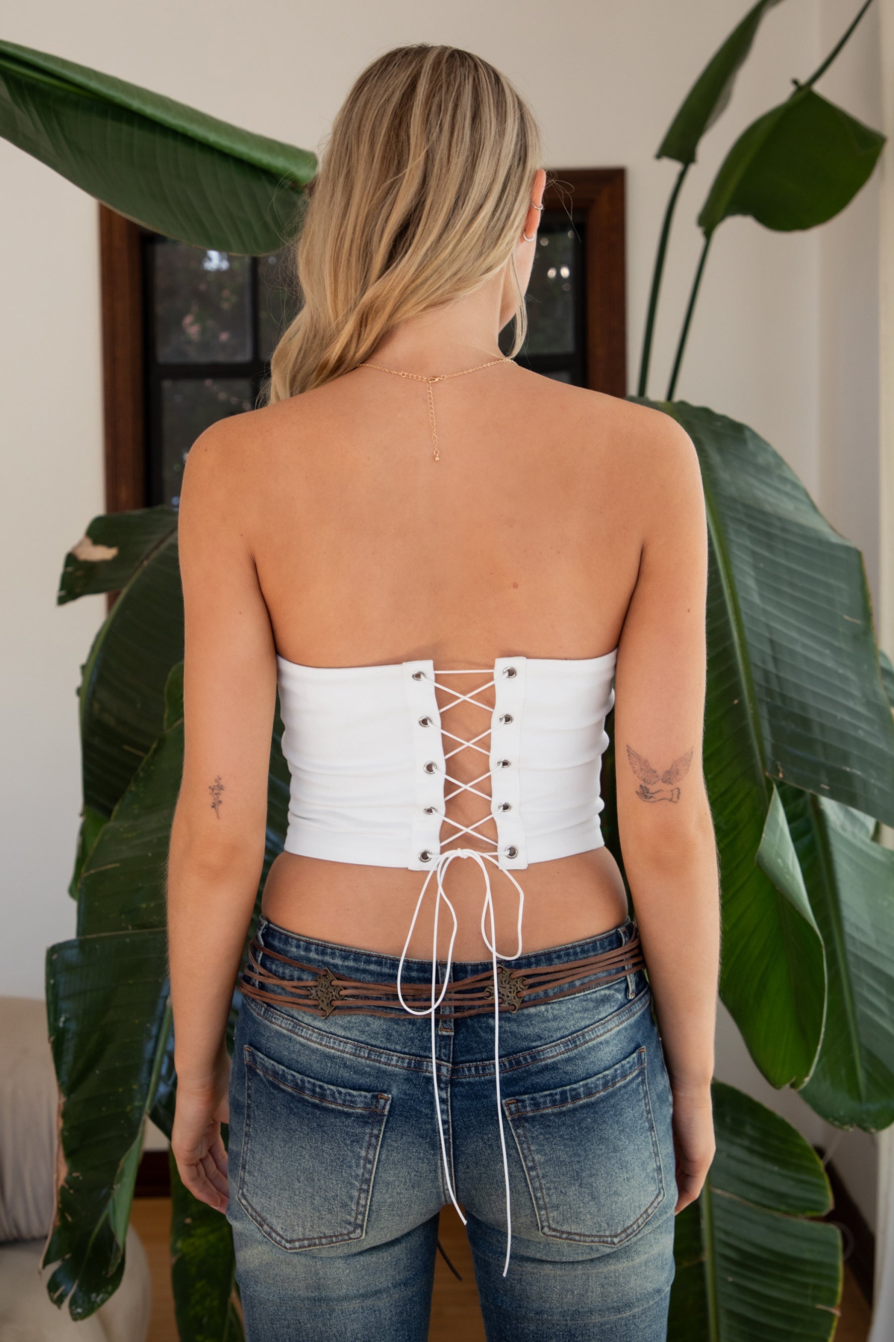 Woman wearing TIC TOC TA31570 HOWDEE white stretch twill strapless bustier top with “Howdy Cowboys” embroidery and rhinestone boot graphic paired with dark denim jeans in an indoor setting