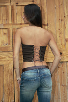 Woman wearing the TIC TOC TA31571 RODEA strapless western bustier top featuring sequin RODEO lettering, horse patch, and lace-up back closure and jeans against a wooden background