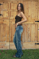 Woman wearing the TIC TOC TA31571 RODEA strapless western bustier top featuring sequin RODEO lettering, horse patch, and lace-up back closure and jeans against a wooden background