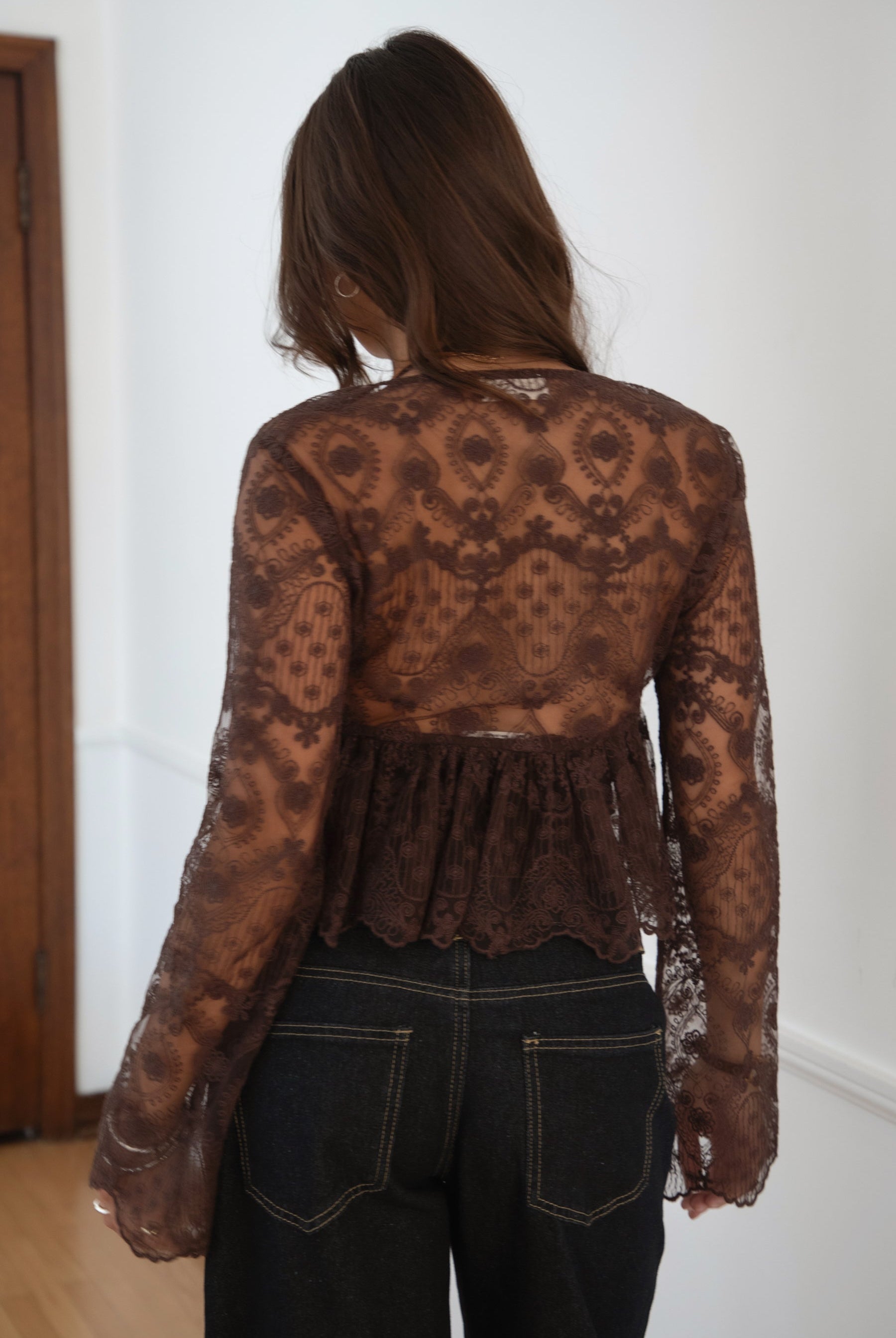 Model wearing the TIC TOC TA31608 LAREDA brown crochet embroidered long sleeve top featuring a scalloped V-neckline, tie front detail, and flowy bell sleeves with dark denim jeans.