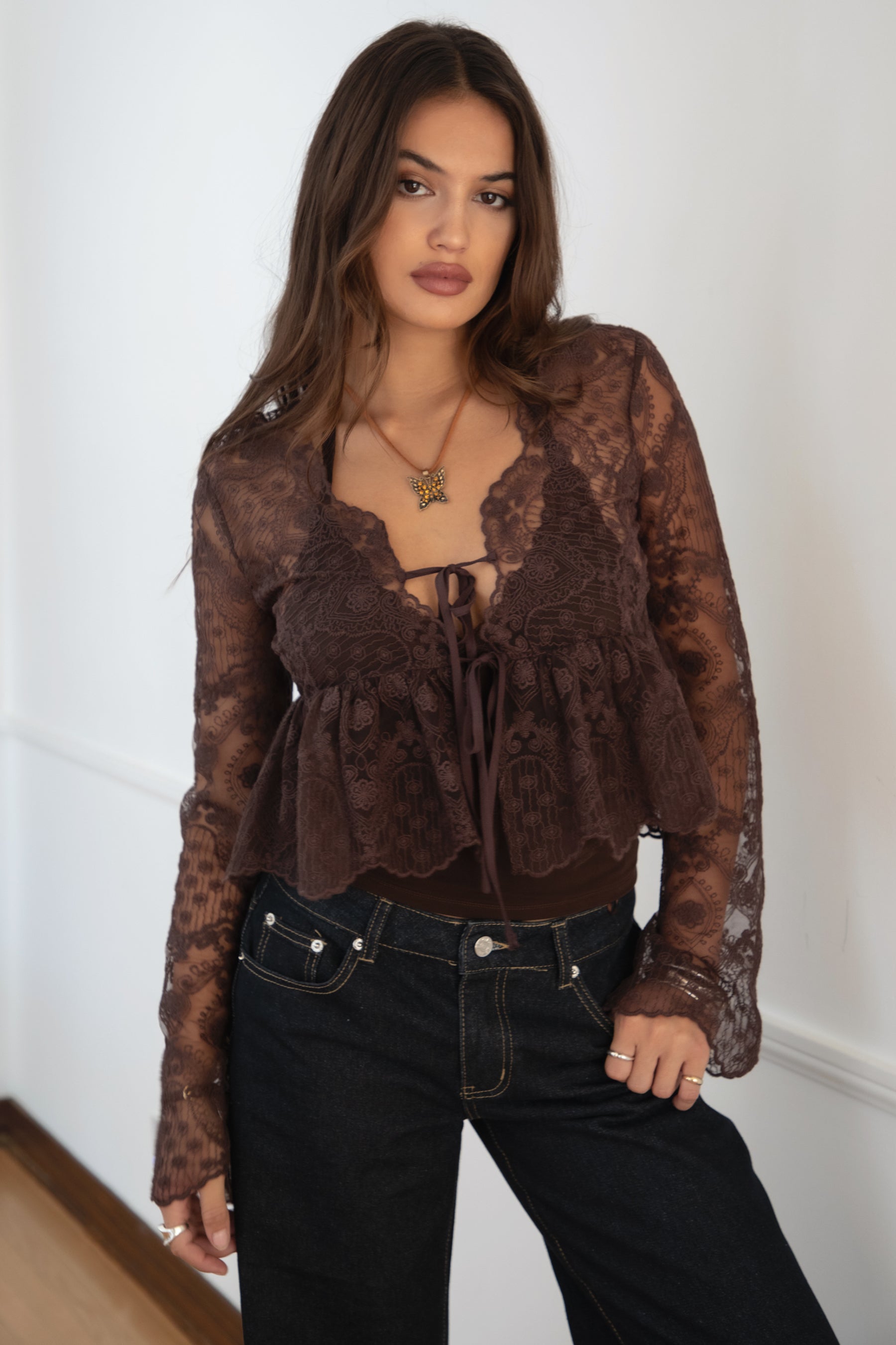 Model wearing the TIC TOC TA31608 LAREDA brown crochet embroidered long sleeve top featuring a scalloped V-neckline, tie front detail, and flowy bell sleeves with dark denim jeans.