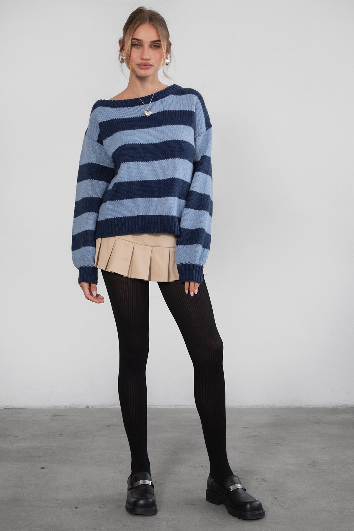 A woman wearing a TIC TOC TC30623 Maddee navy blue rugby knit oversized sweater with an off-the-shoulder neckline and striped color block design, paired with a beige skirt