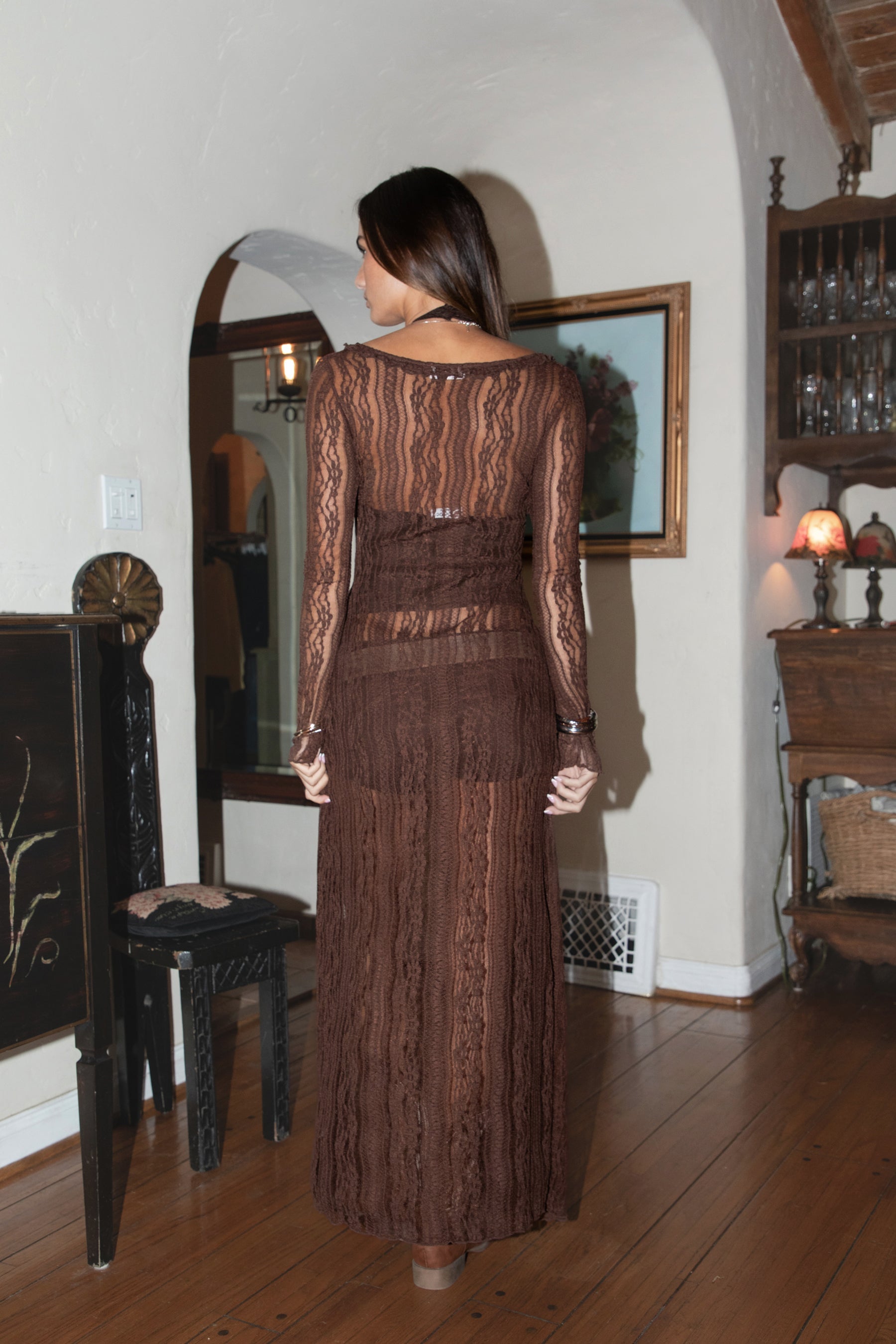 Woman wearing a brown lace duster standing in a room with wooden floors and a mirror.
