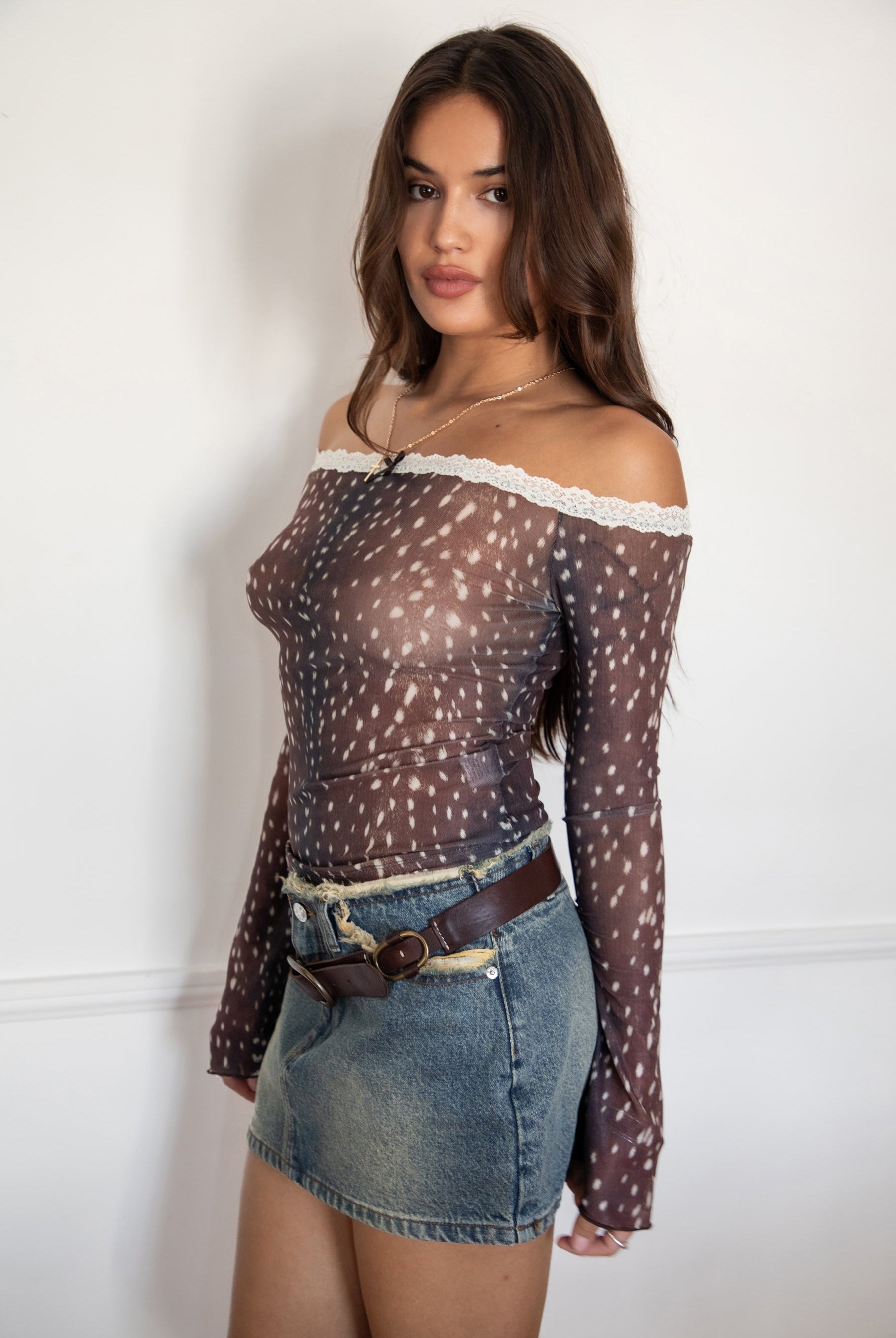 Woman wearing the TIC TOC TC31579 BAMBELLE off-the-shoulder top featuring a deer-inspired mesh print, lace trim neckline, and long bell sleeves paired with a distressed denim mini skirt