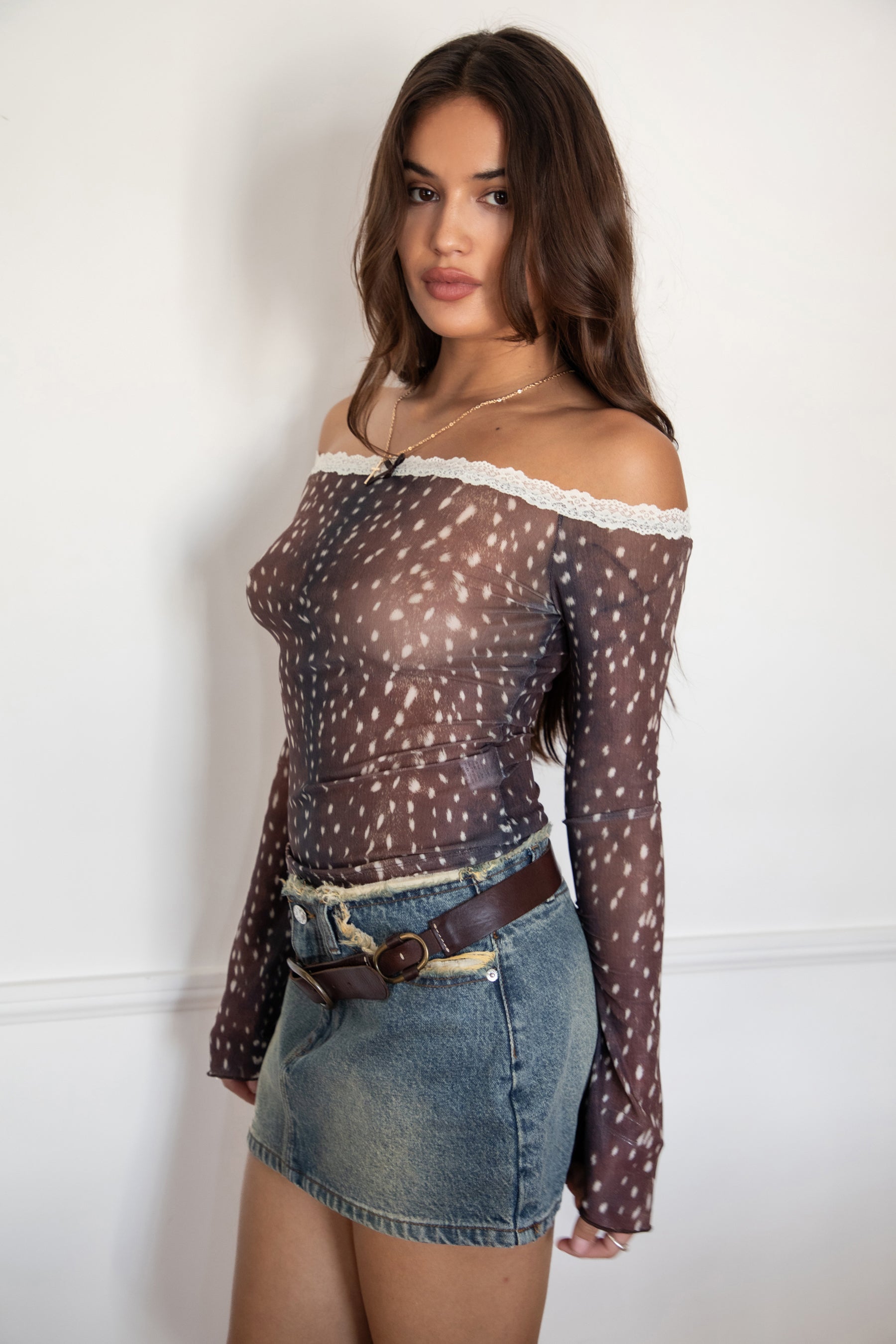 Woman wearing the TIC TOC TC31579 BAMBELLE off-the-shoulder top featuring a deer-inspired mesh print, lace trim neckline, and long bell sleeves paired with a distressed denim mini skirt