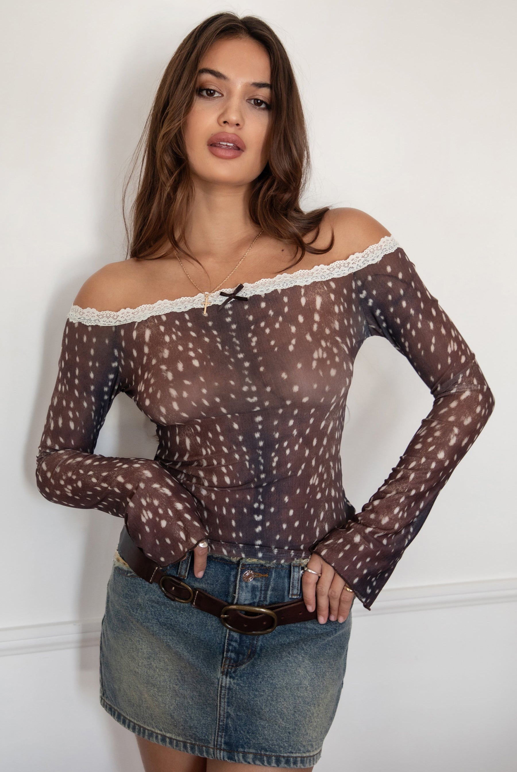 Woman wearing the TIC TOC TC31579 BAMBELLE off-the-shoulder top featuring a deer-inspired mesh print, lace trim neckline, and long bell sleeves paired with a distressed denim mini skirt