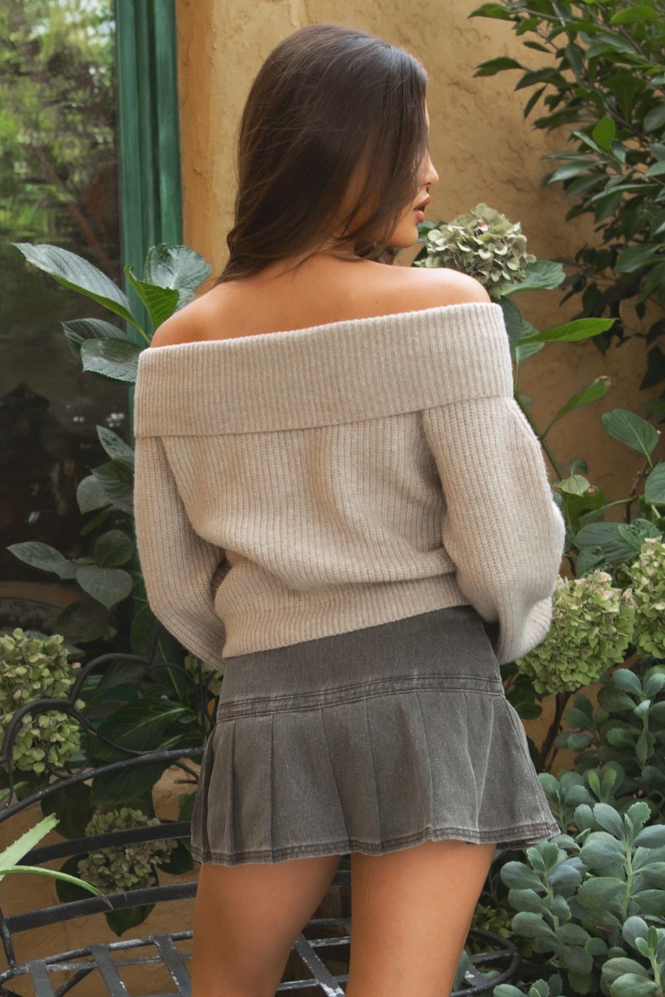 Woman wearing the TIC TOC TC31658 HAZE beiger knit off the shoulder sweater featuring a foldover neckline, ribbed cuffs, and relaxed fit paired with a brown denim skirt outdoors.