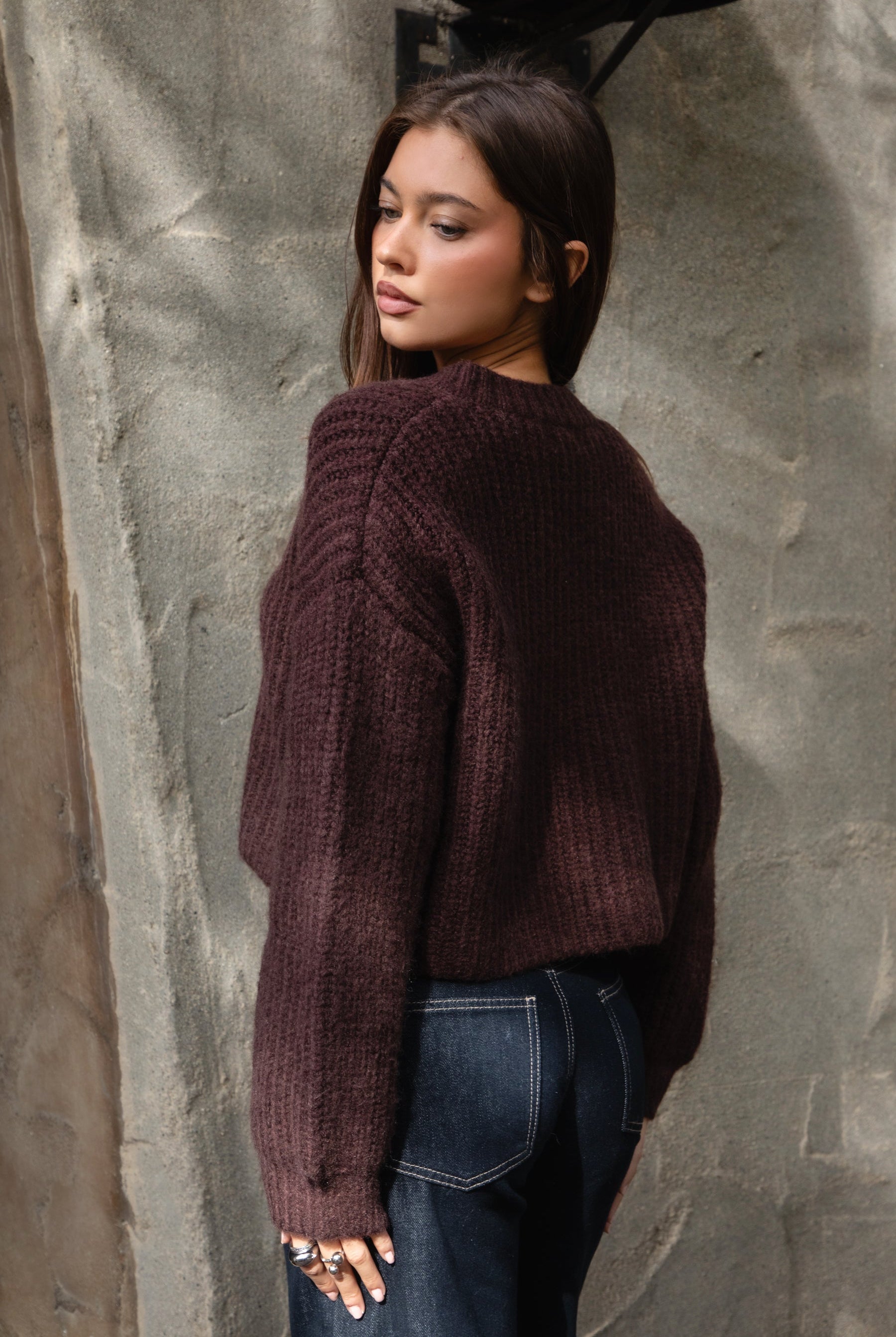 Woman wearing TIC TOC TF31833 ISOLDE brown wool-blend button down cardigan with boxy cropped fit, ribbed trim, and marled knit texture paired with dark jeans against a textured wall.