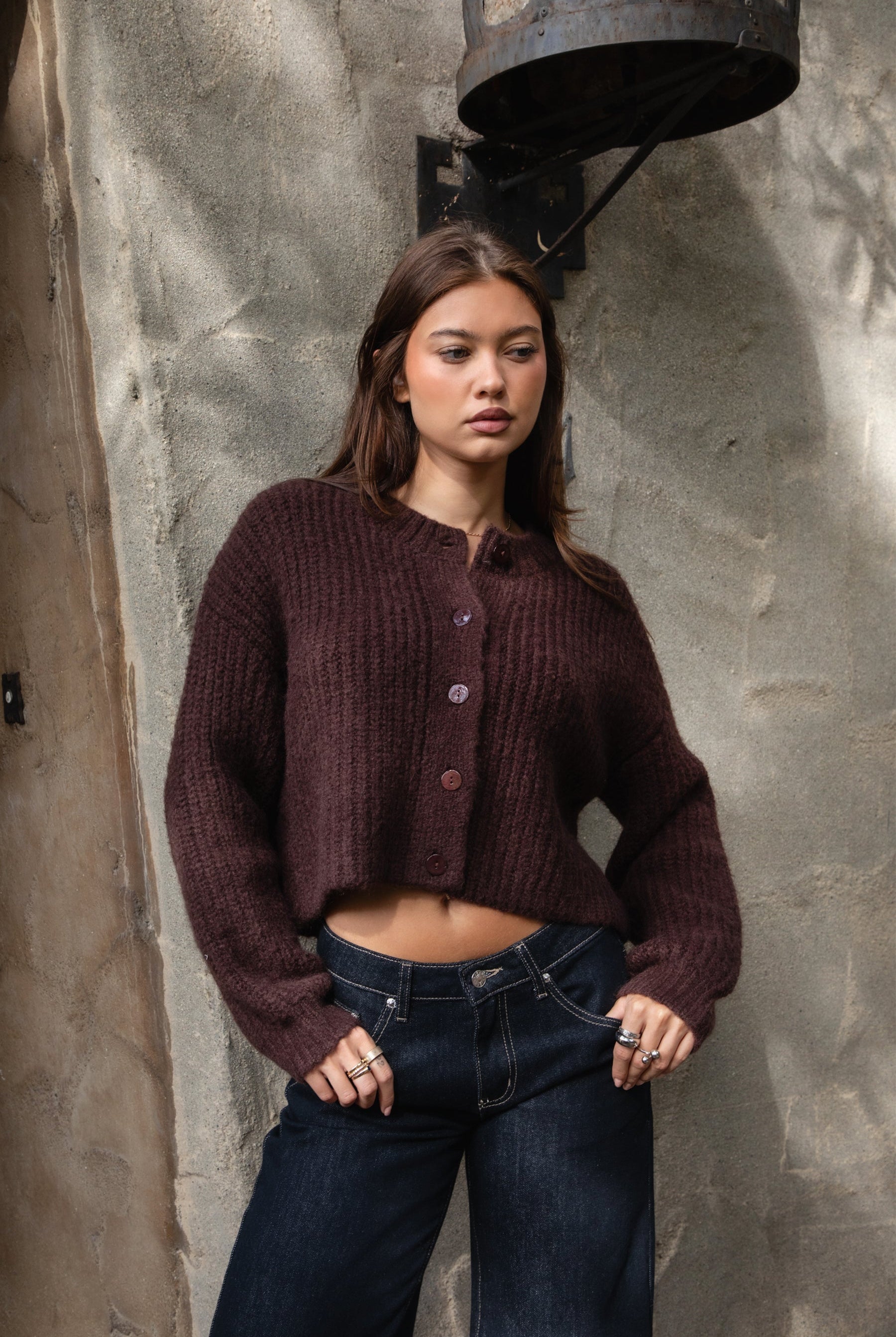 Woman wearing TIC TOC TF31833 ISOLDE brown wool-blend button down cardigan with boxy cropped fit, ribbed trim, and marled knit texture paired with dark jeans against a textured wall.