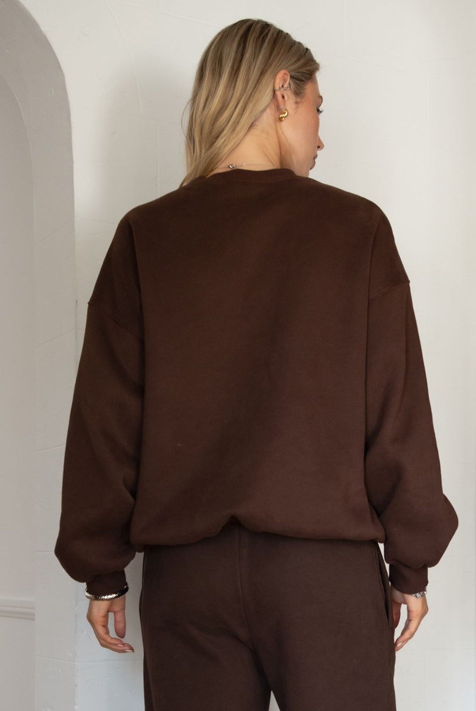 Person wearing a brown sweatshirt and pants in a minimalistic setting