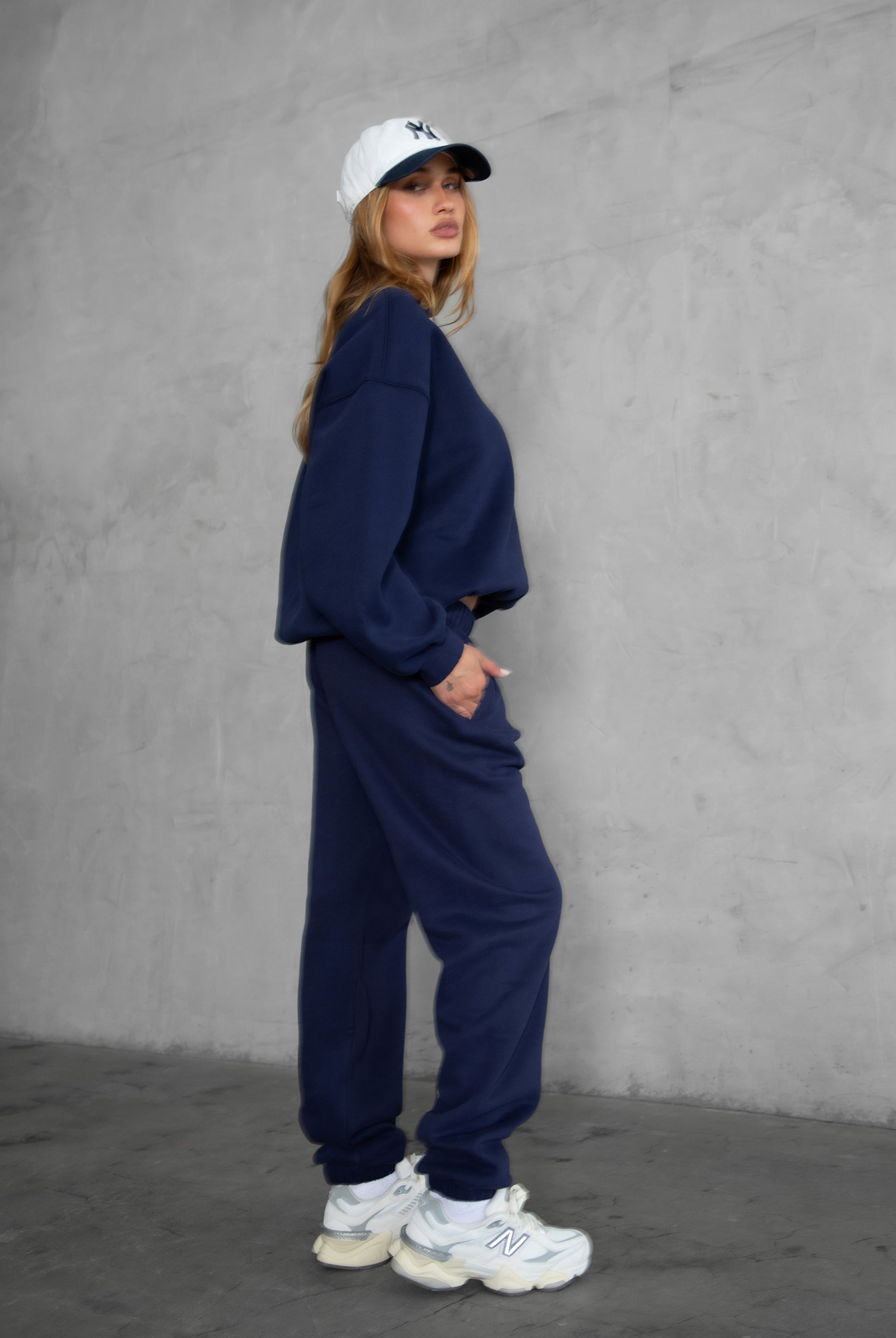 Person wearing a navy tracksuit and white sneakers against a gray background