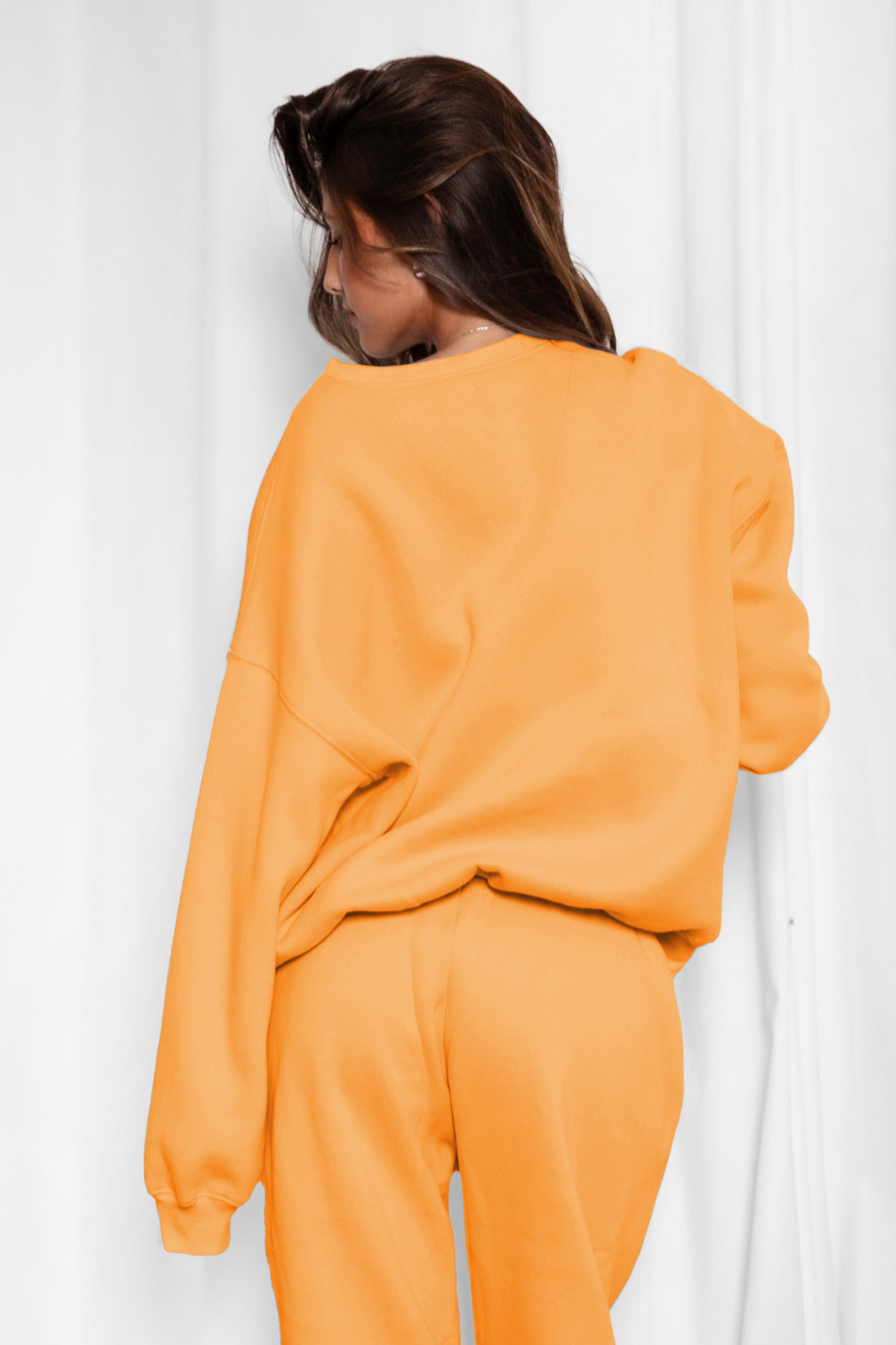 Person wearing an orange outfit against a white curtain background